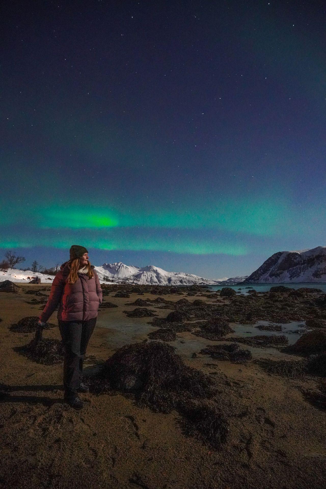 Lydia standing on a beach with the Northern Lights behind her