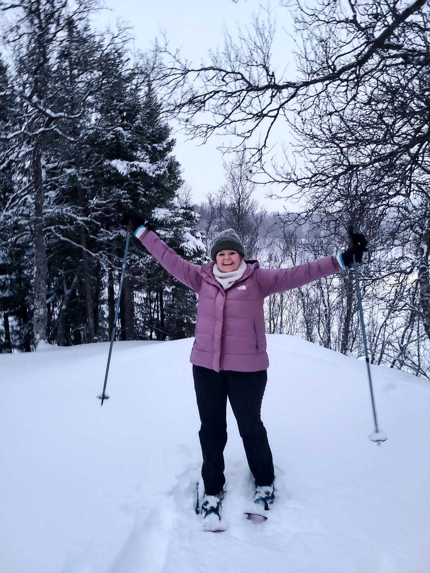 Lydia holding poles up on the air while snowshoeing in Tromso. She wears a purple puffer coat