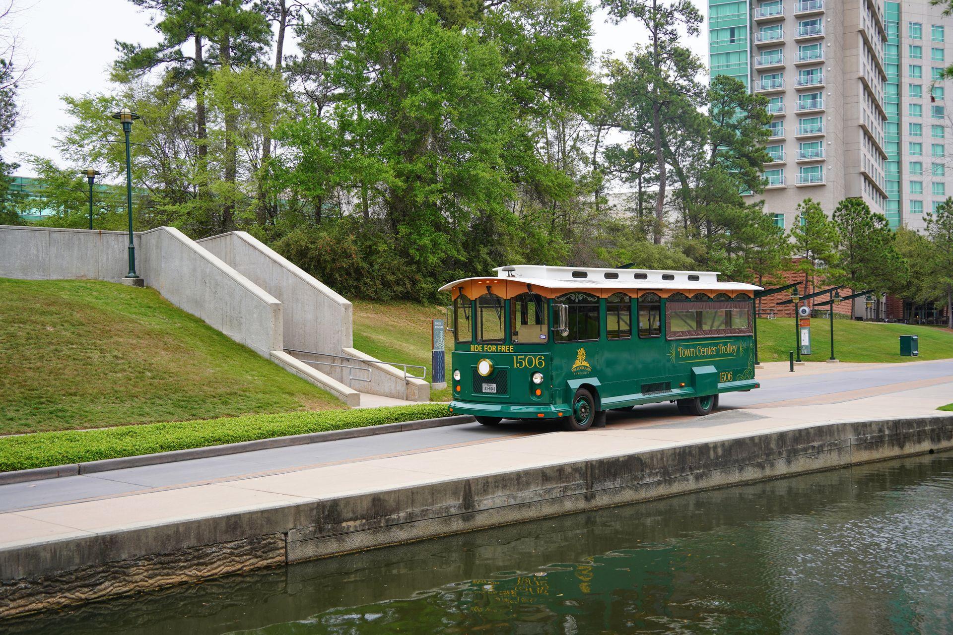 A green trolley driving along The Waterway in The Woodlands