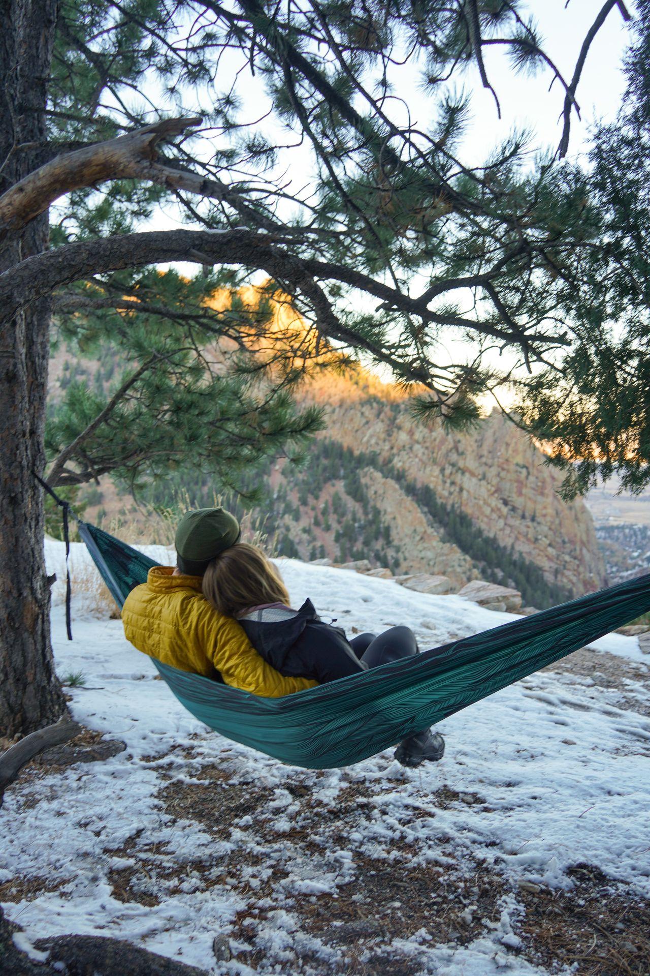 Lydia and Joe sitting in a hammock and looking out a sunsest with snow on the ground.