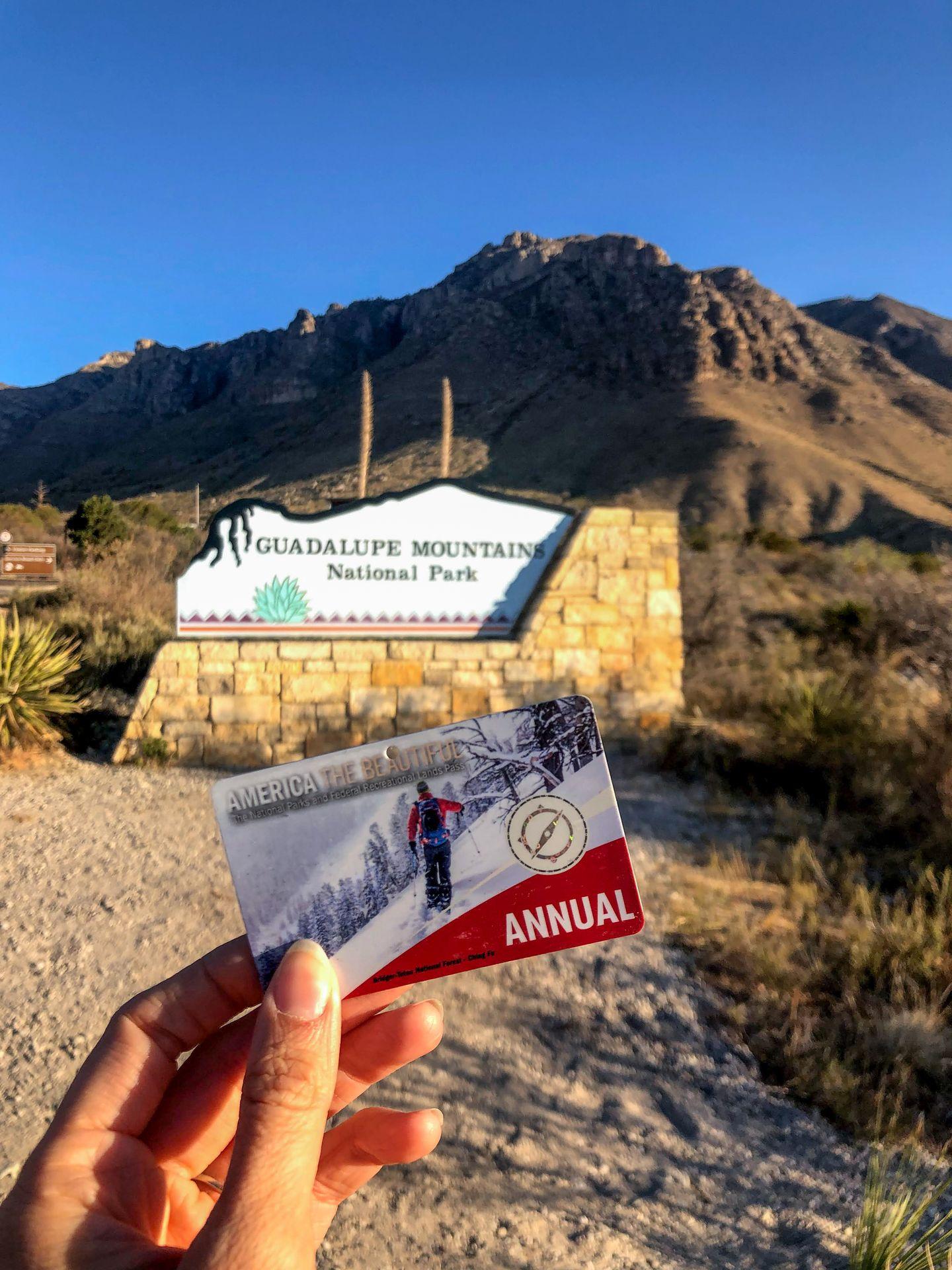 Holding up an America the Beautiful Pass in front of the park sign at Guadalupe Mountains National Park.
