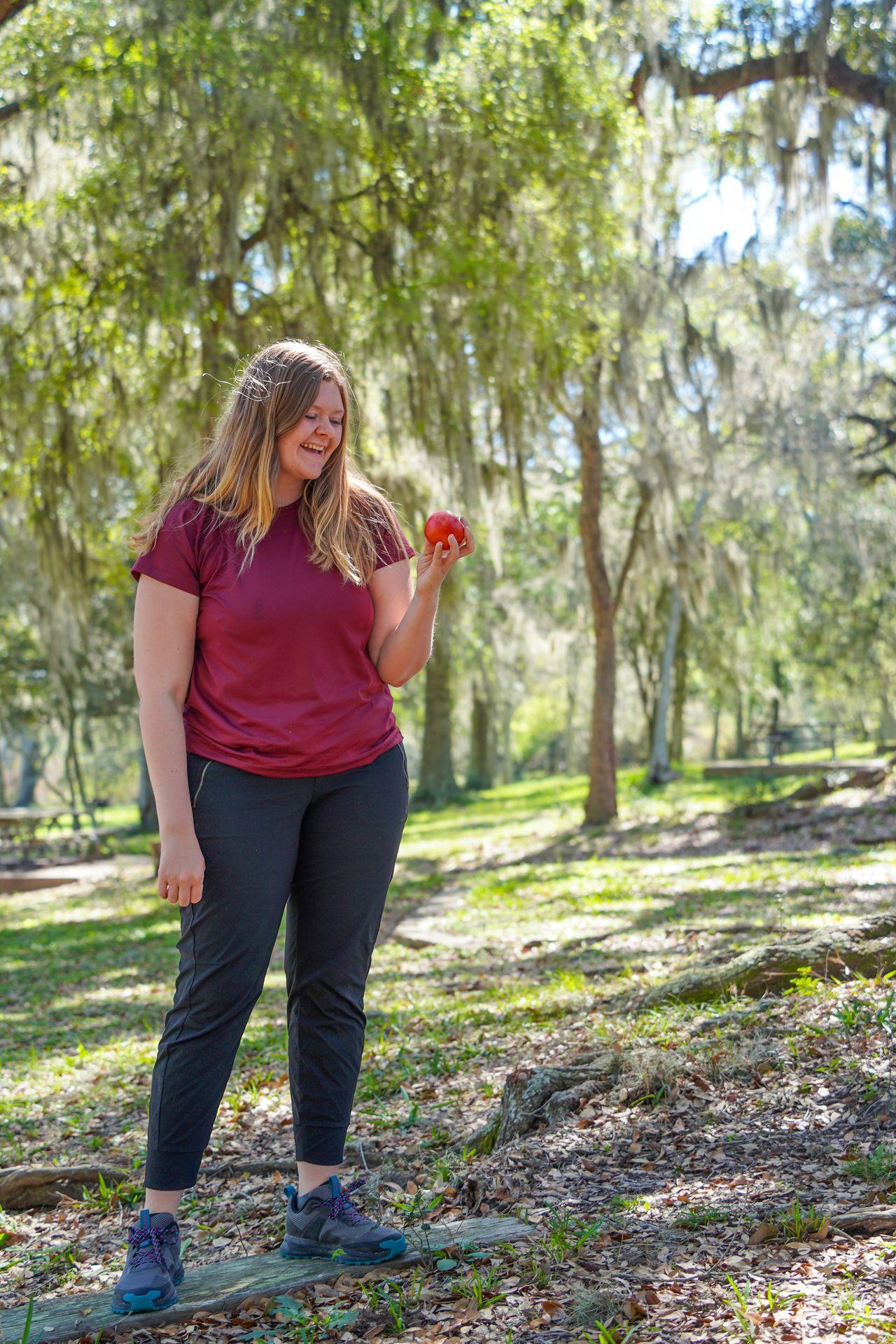 Lydia standing under trees with hanging moss in Texas. She holds a red apple.