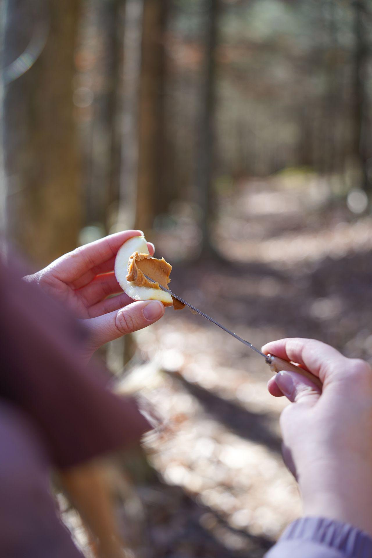 Spreading peanut butter on a slice of apple while on a hike.
