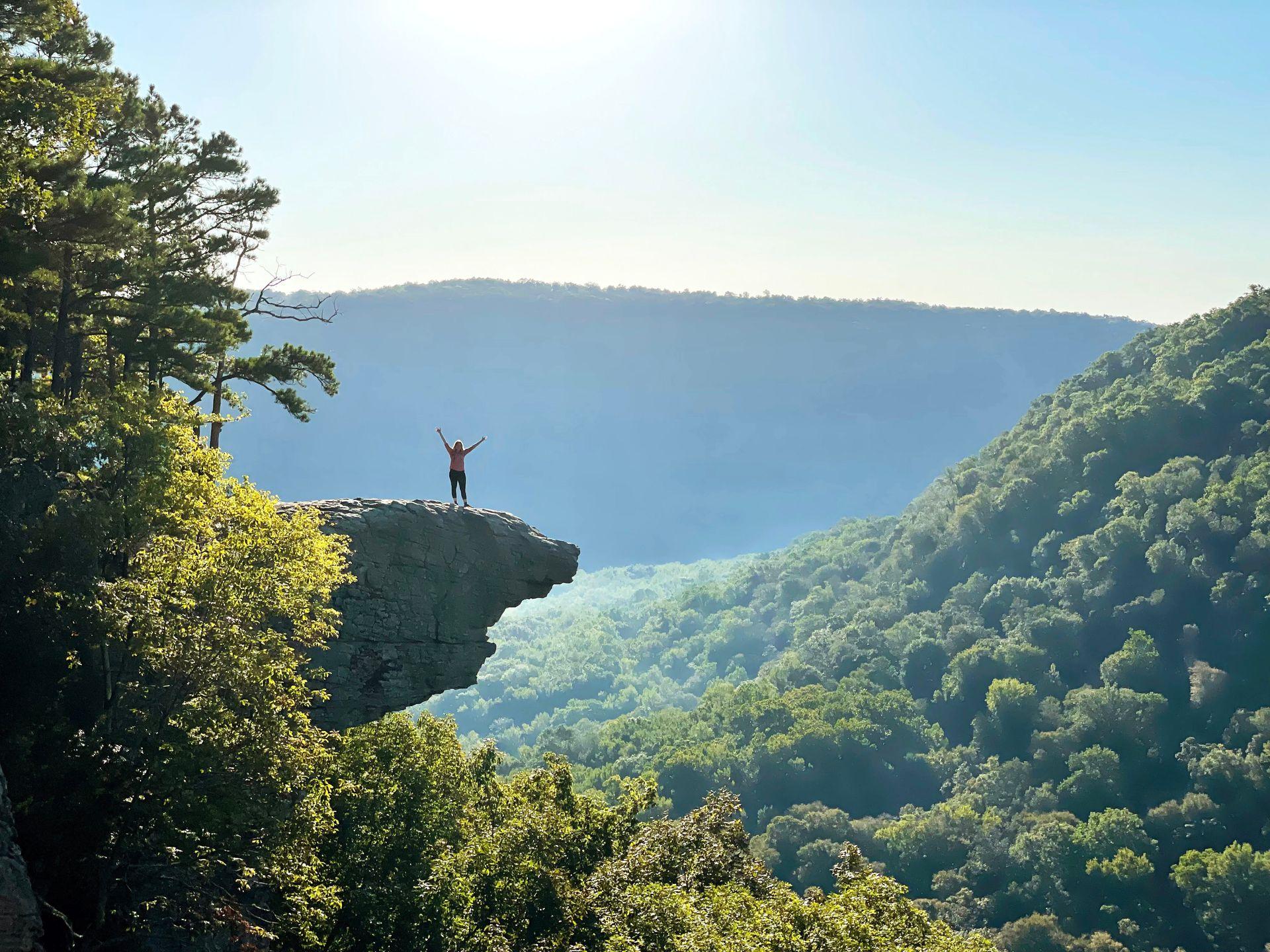 Lydia standing on Hawkbill Crag/Whitaker Point in Arkansas. She is far away and has her hands up in the air.