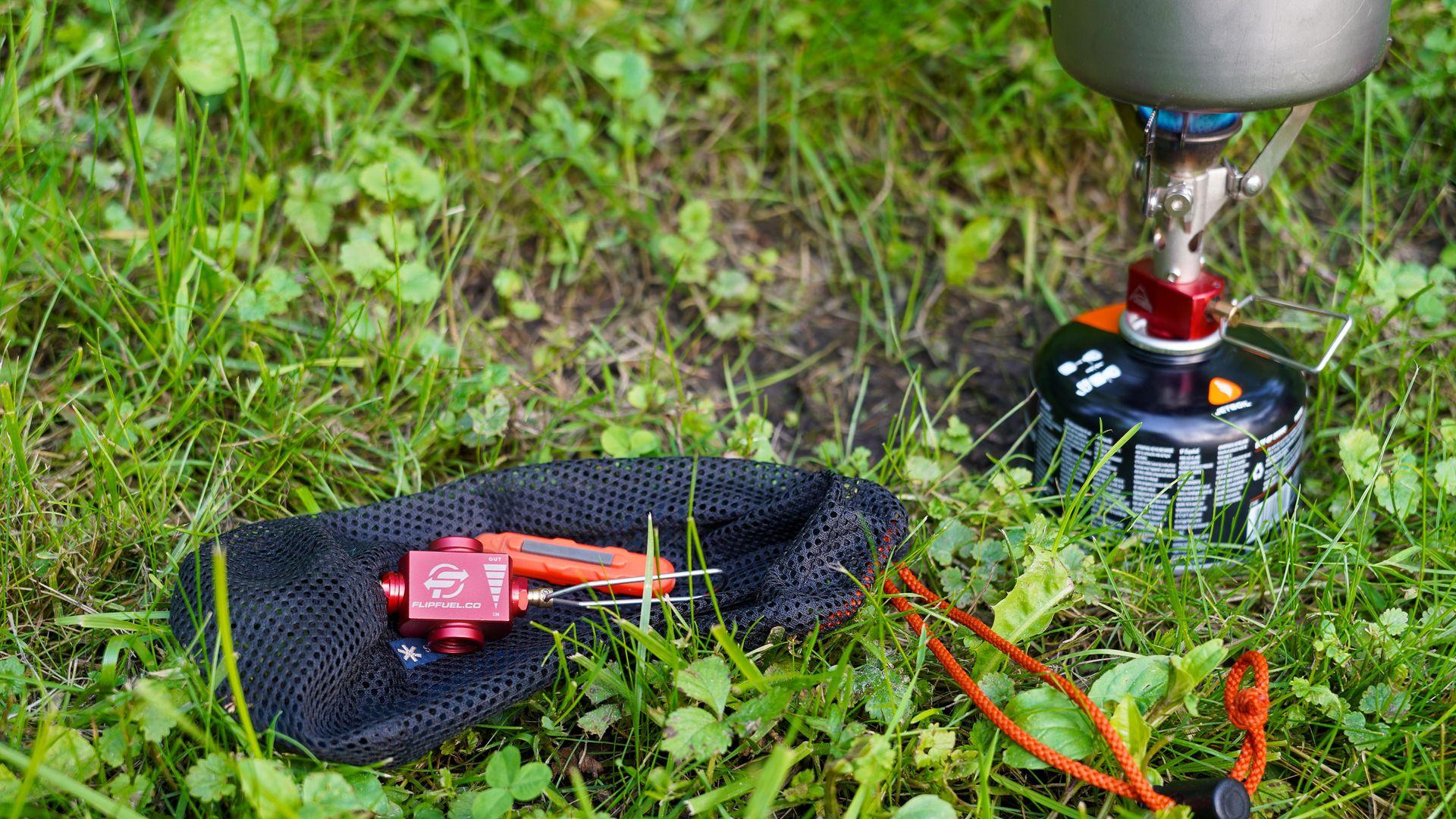 A FlipFuel sits on a bag in the grass next to FlipFuel being used to transfer fuel.