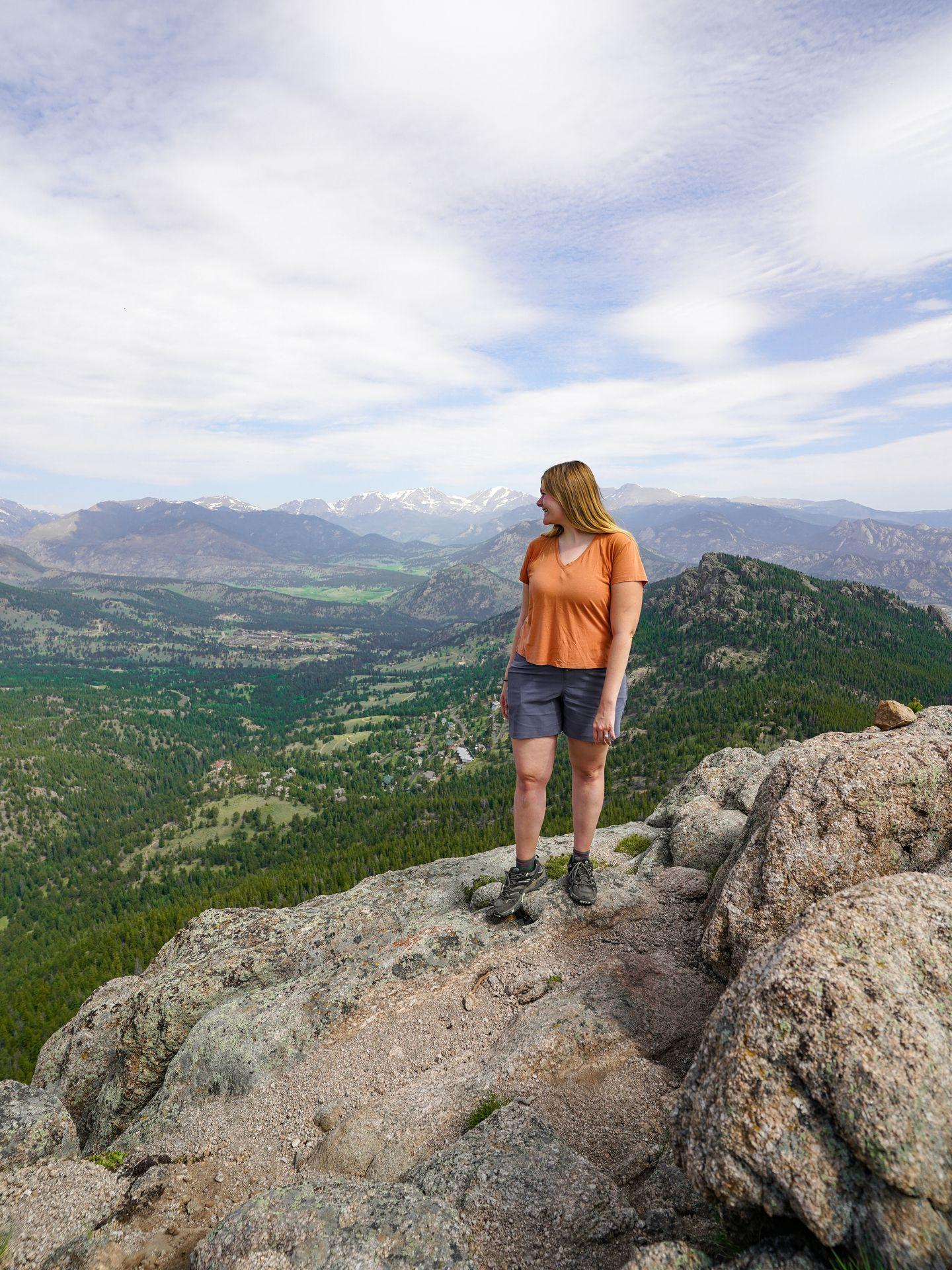 Lydia standing on a rocky mountain top wearing an orange shirt and blue shorts
