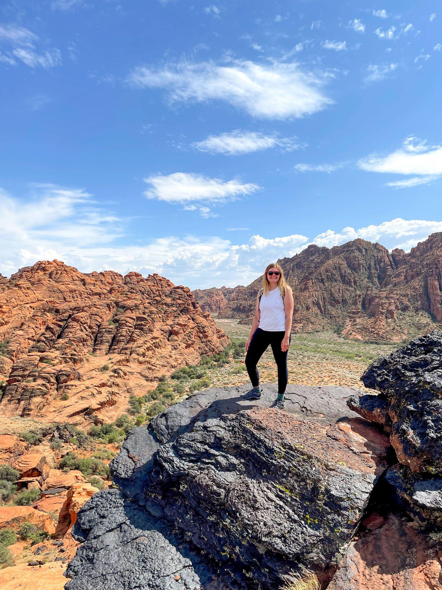 Lydia standing on a black rock with an orange canyon behind her.
