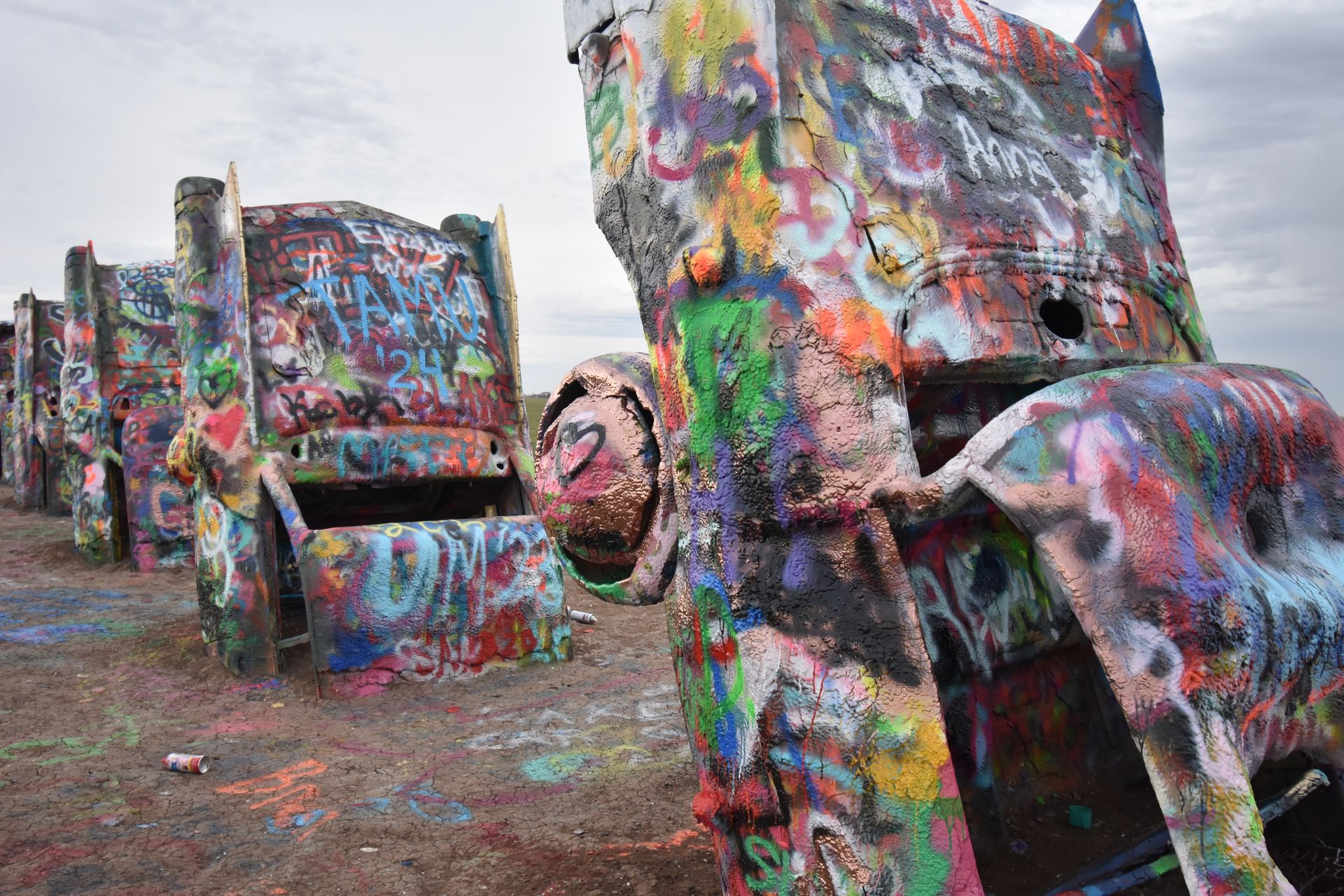 Four Cadillacs sticking up out of the ground and covered with many layers of spray paint.