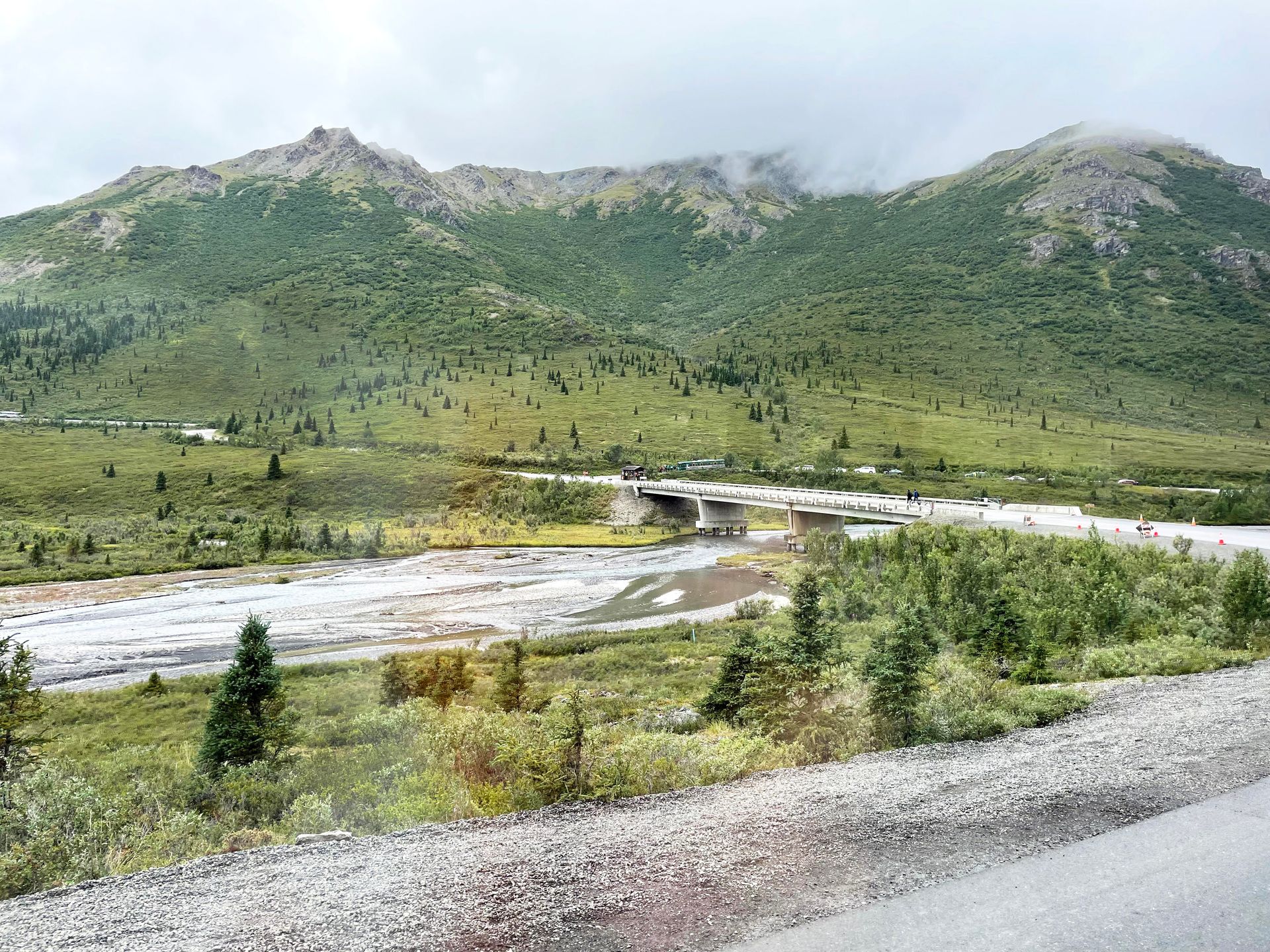 A bridge going over a river and green mountains obscured in a bit of fog in Denali National Park