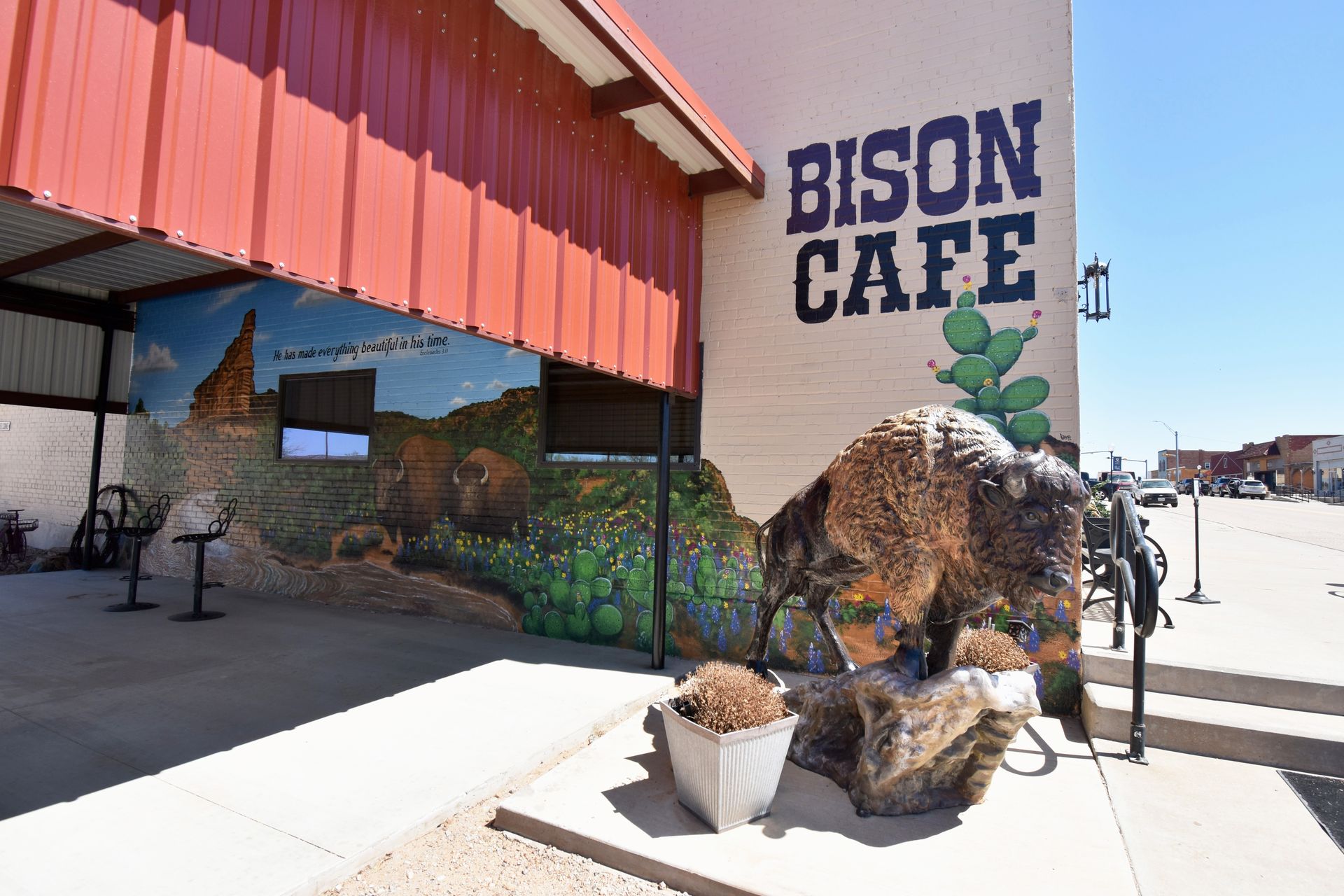 A bison statue in front of a buildng labeled "Bison Cafe." On the building is a mural painted with cacti and bison.