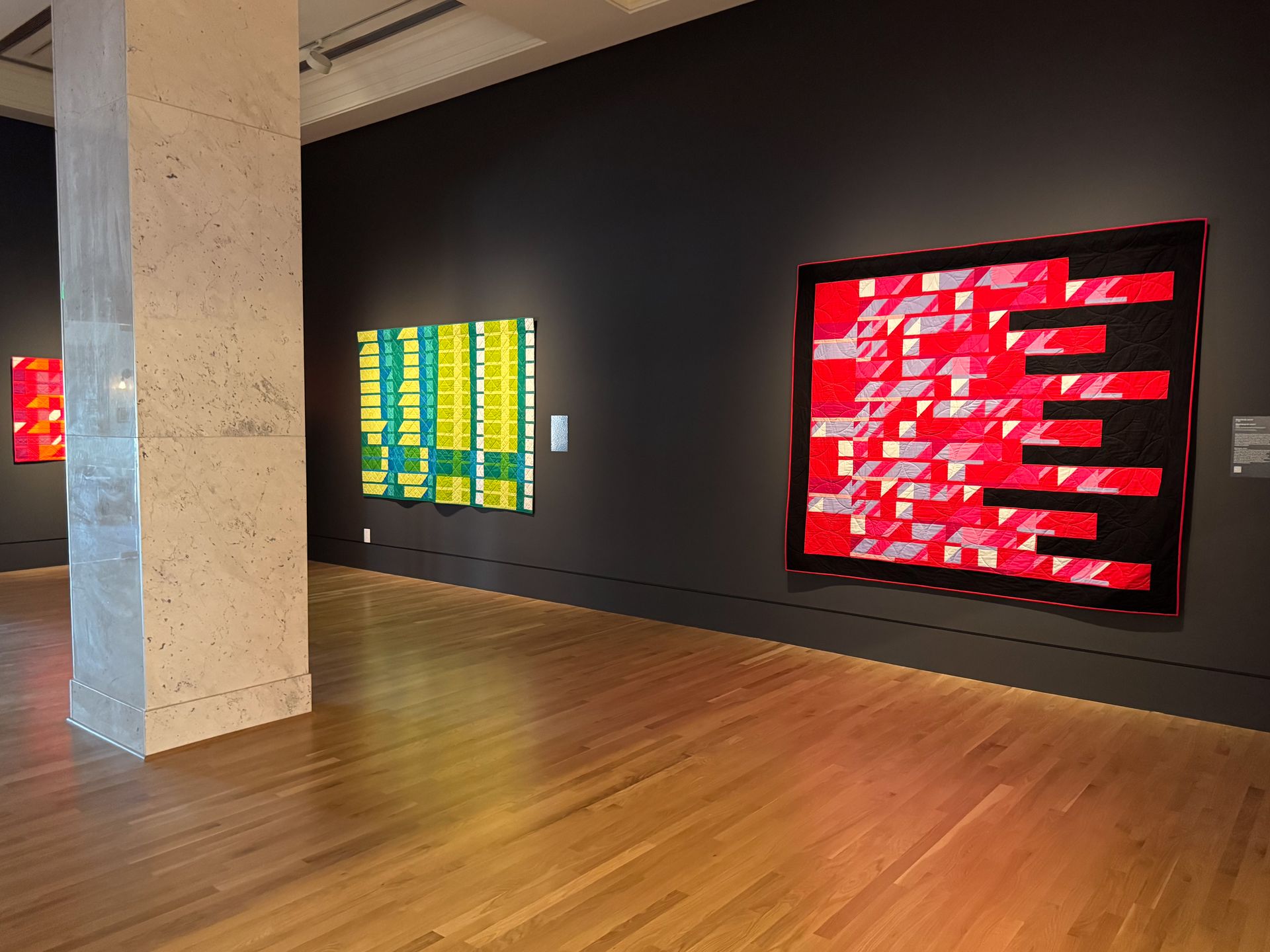 Vibrant red and green quilts hanging up in the Museum of Nebraska Art