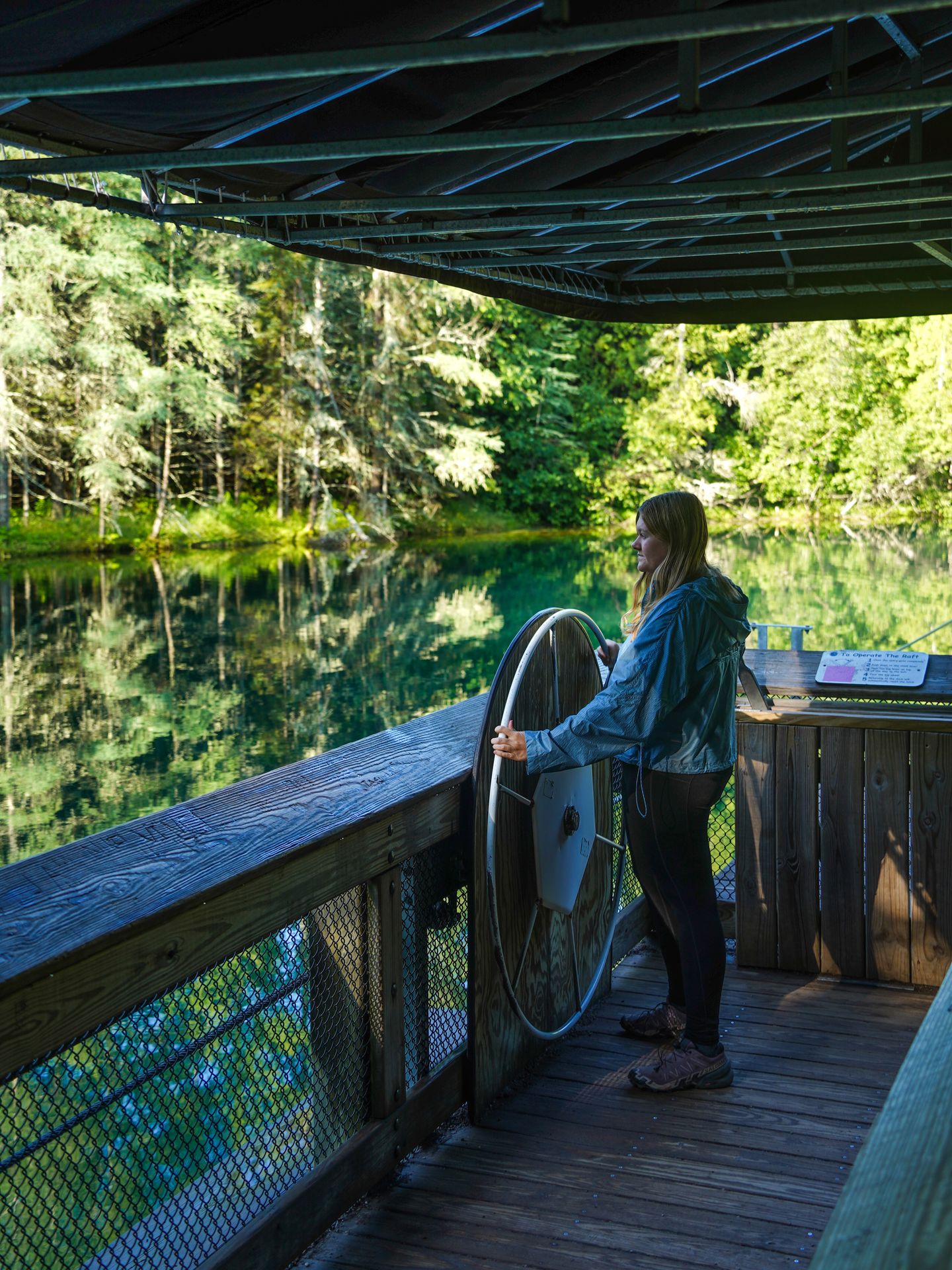 Lydia standing at a large steering wheel on the raft at Kitch-iti-kipi