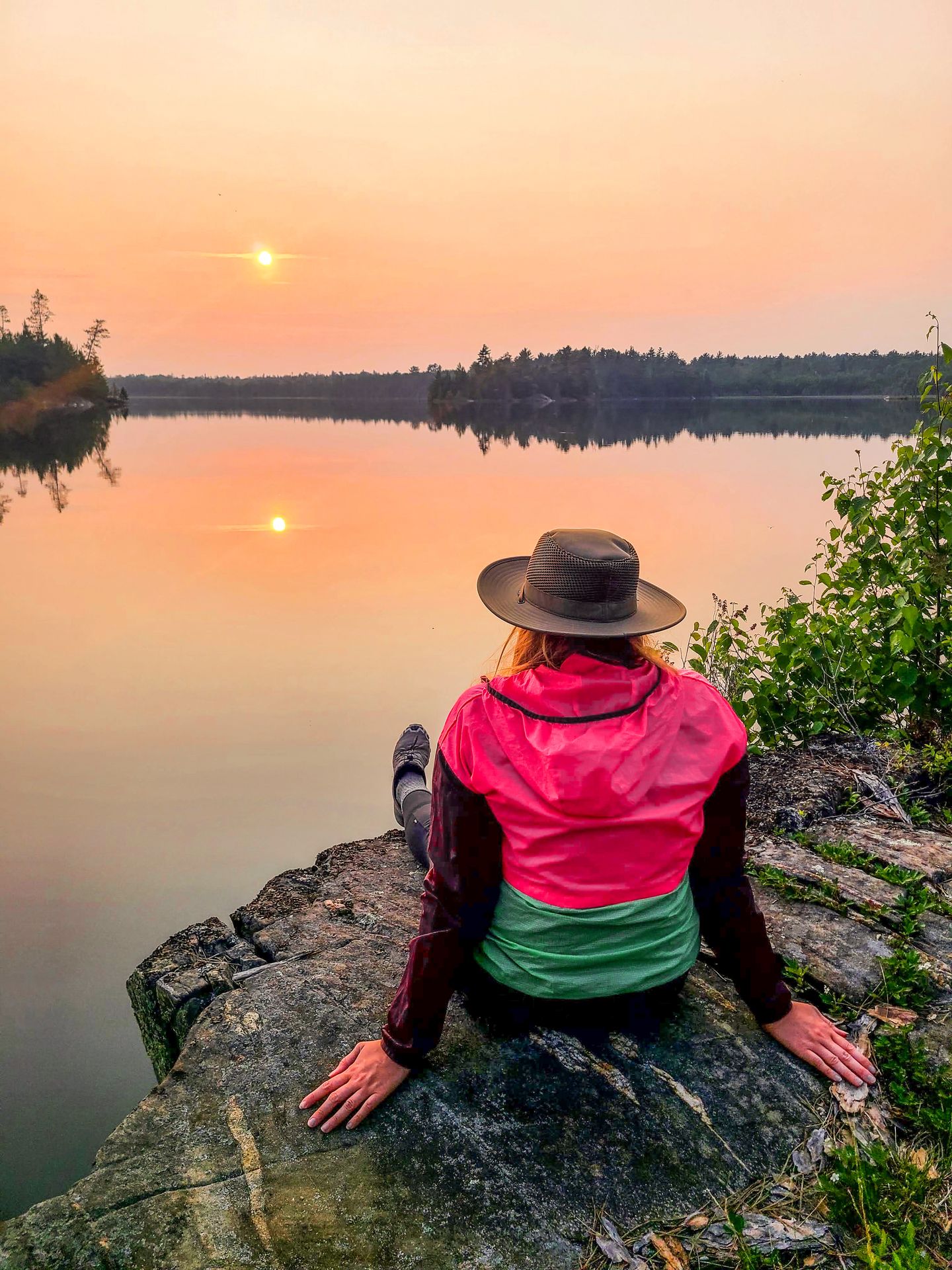 Lydia sitting on a rock and watching the sunset over a lake in Voyageurs National Park
