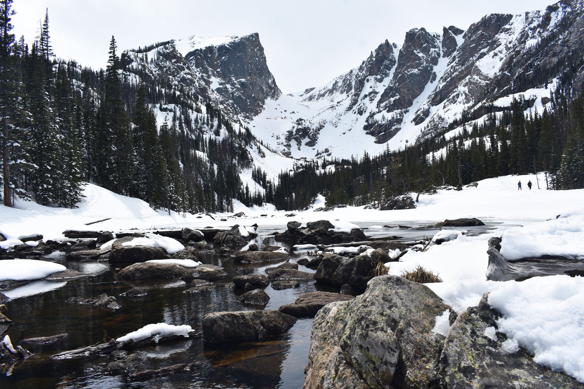 A rocky lake with mountains up above, all covered in snow