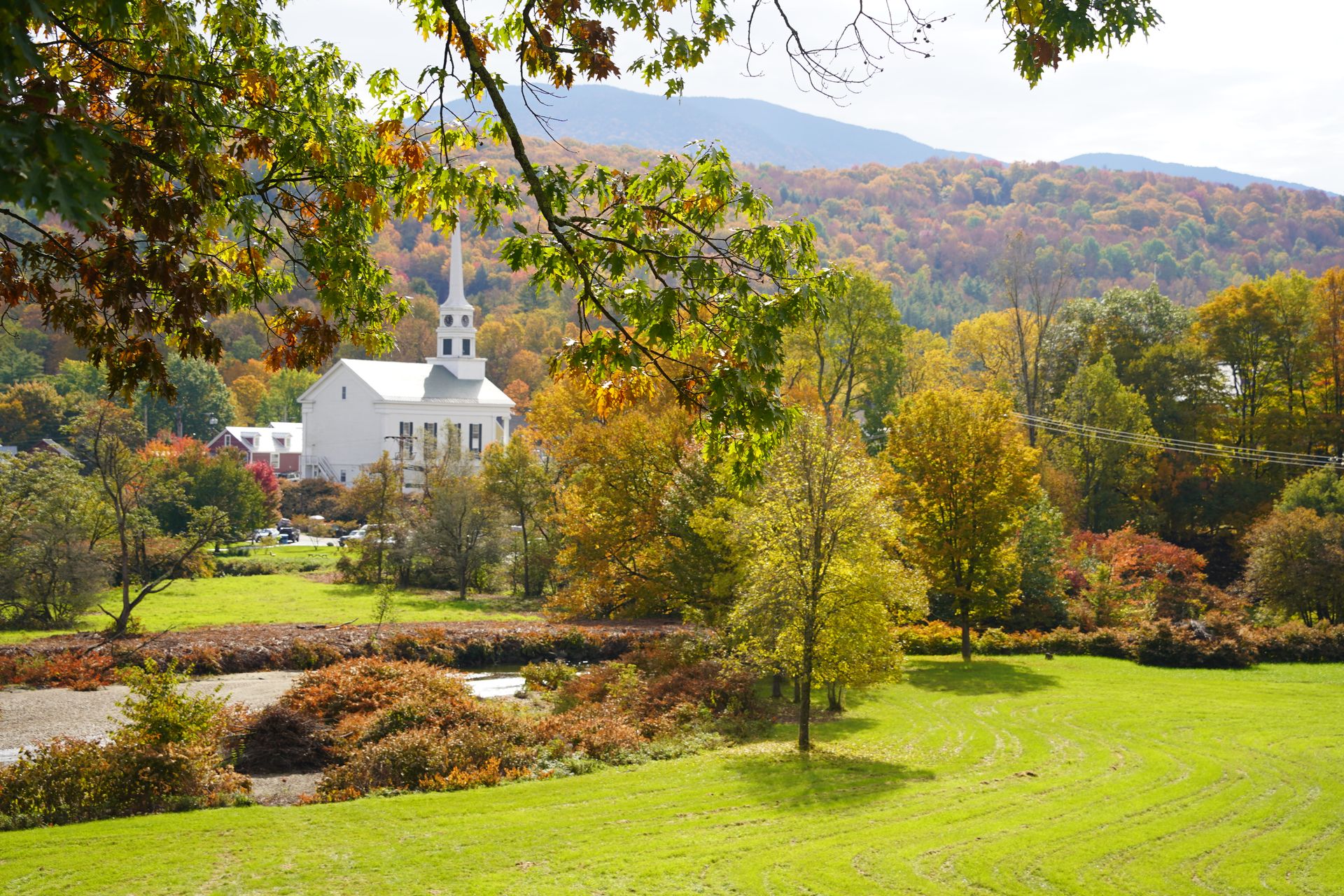 A white church with mountains in the background and trees in the foreground.
