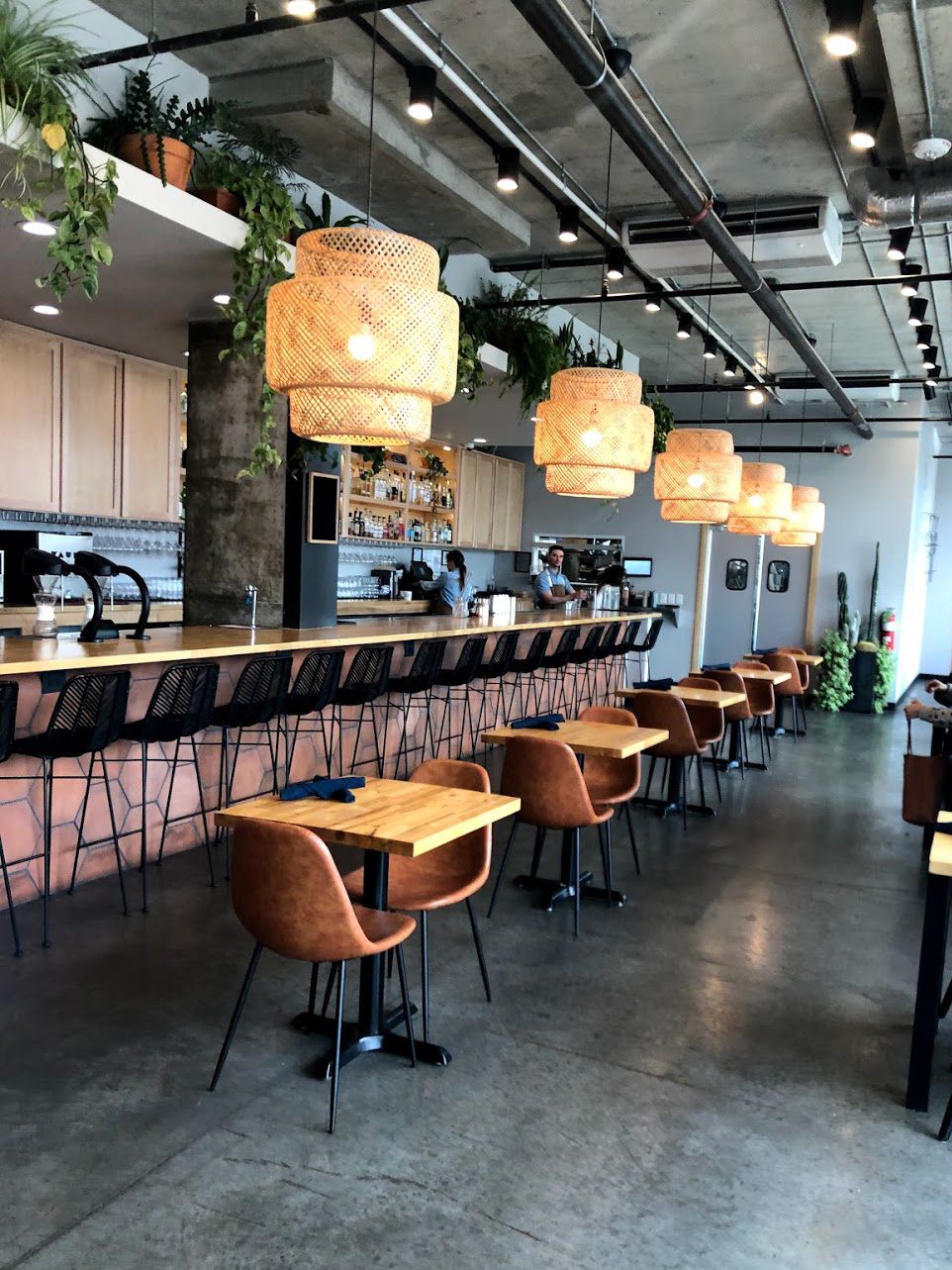 A pink bar with small tables next to it. There is a row of neutral, hanging lights above the bar.