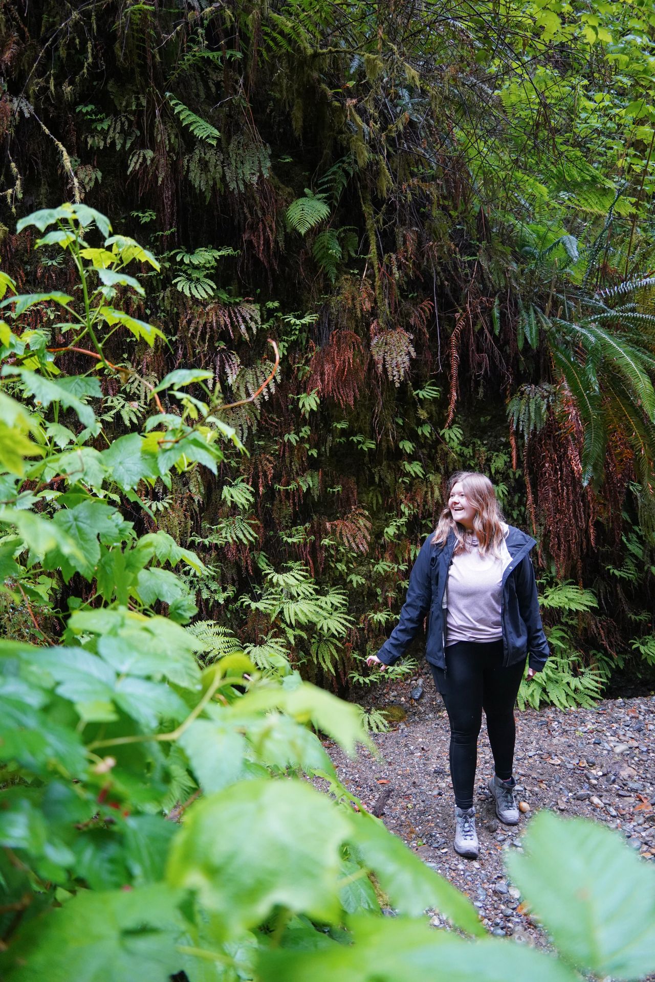 Lydia next to a fern-covered canyon wall on the Fern Canyon Loop