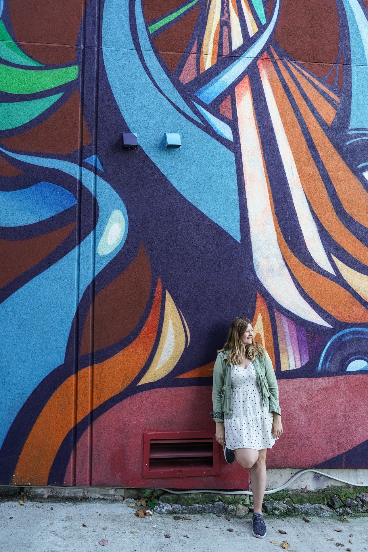 Lydia leaning against a colorful mural at the Punto Urban Art Museum