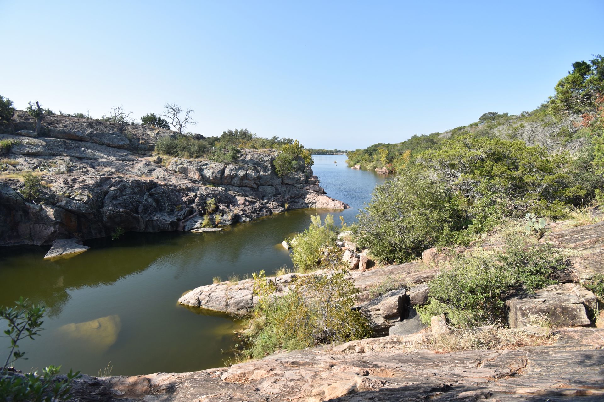 Inks Lake winding back into a cove. The water is surrounded by small, rocky ledges and green trees.