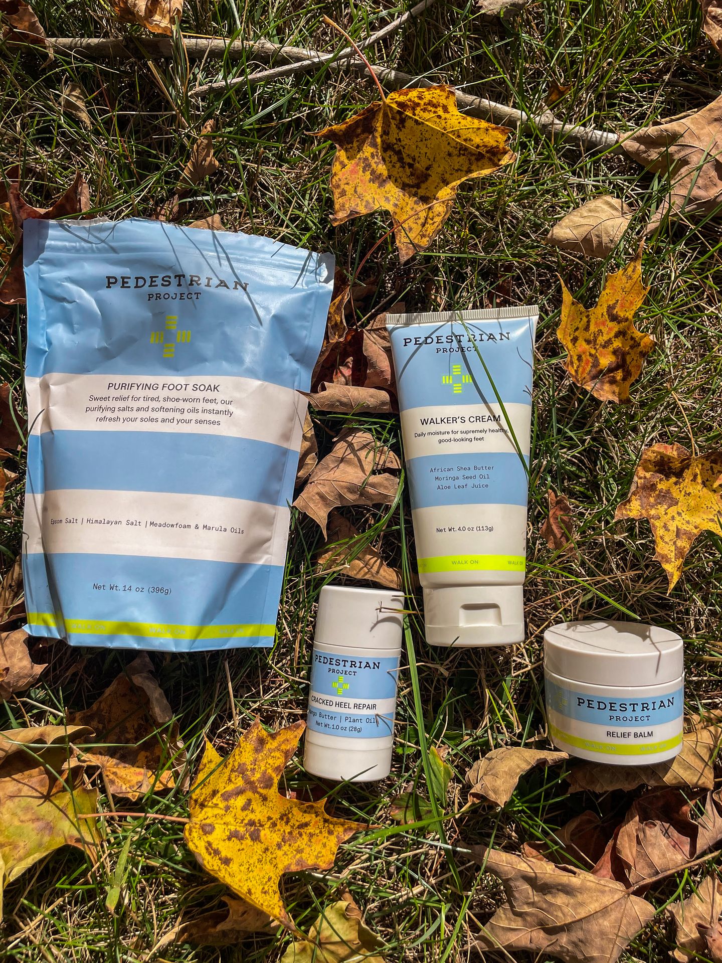 Four Pedestrian Project products placed among dry leaves in grass.