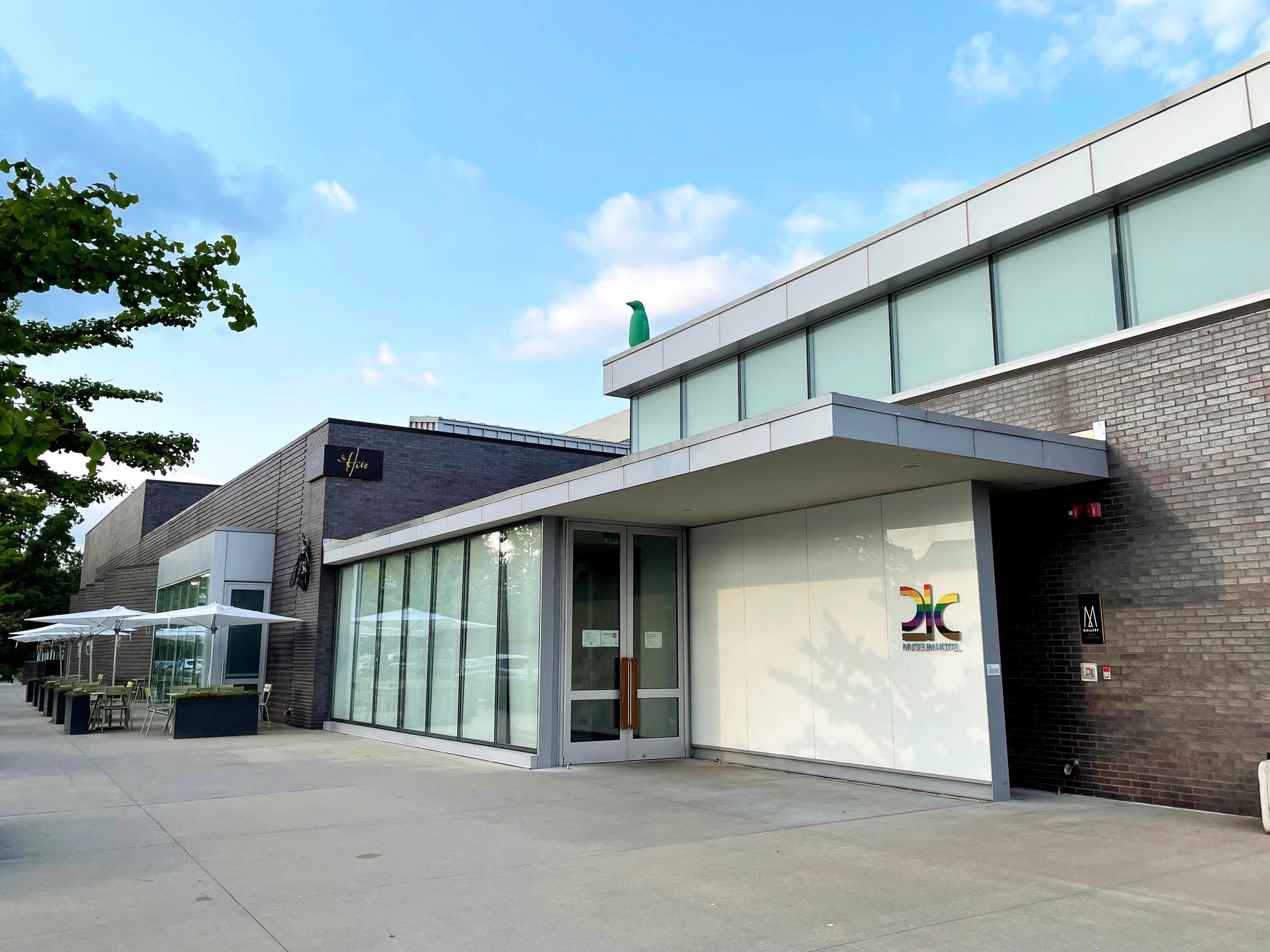 The exterior of the Bentonville 21C. There is a green penguin on the roof and a rainbow 21C label on the window.