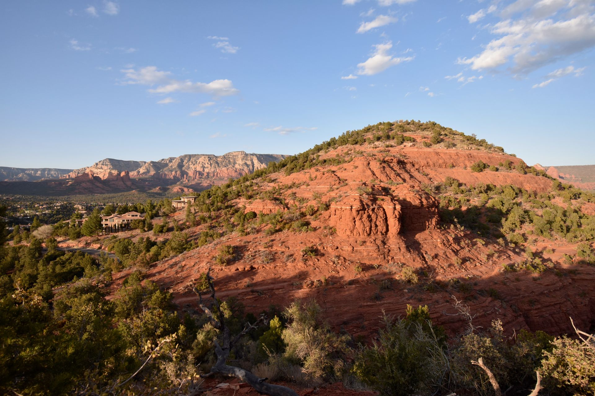 A small orange mountain next to the city of Sedona. There is a larger orange cliff in the distance.