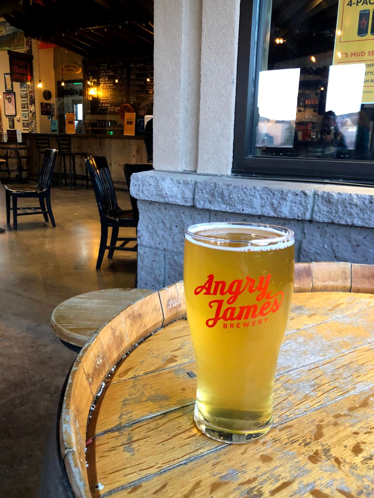 A golden colored beer sitting on a barrel in Angry James Brewery.