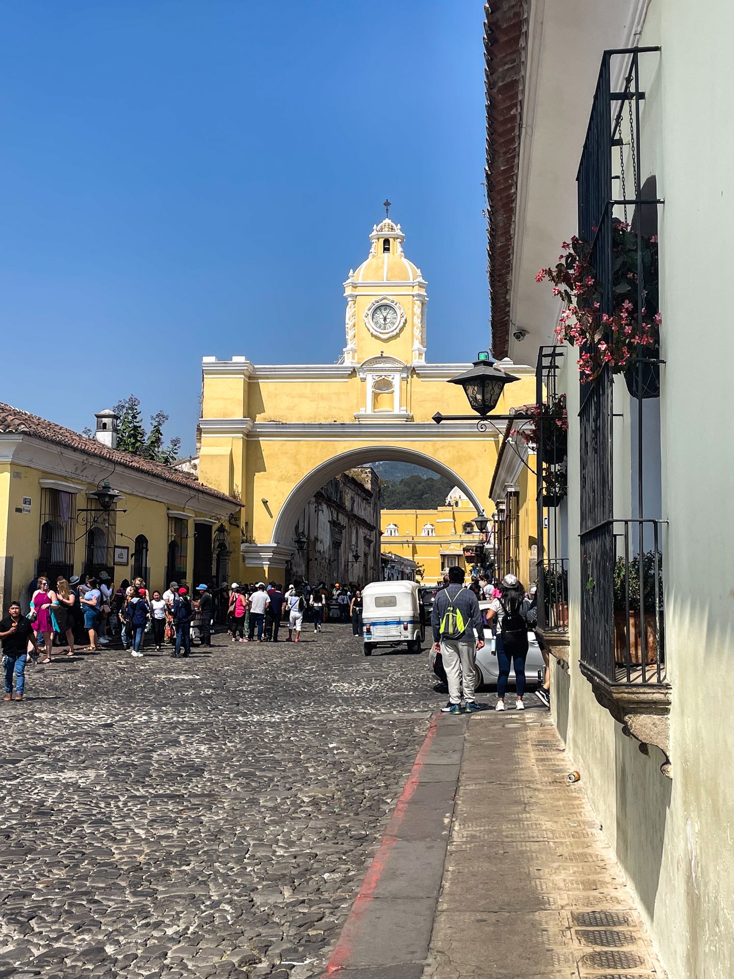 The Santa Catalina Arch in Antigua, which is yellow with a clock tower in the center. There is a stone road below.