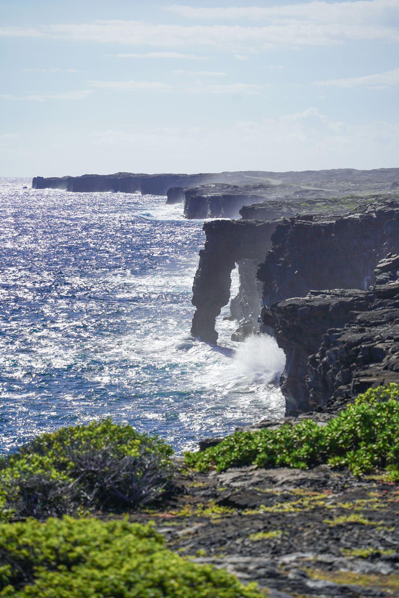 A black rock arch on the coast in Hawaii Volcanoes National Park. Ocean waves request up against the shore