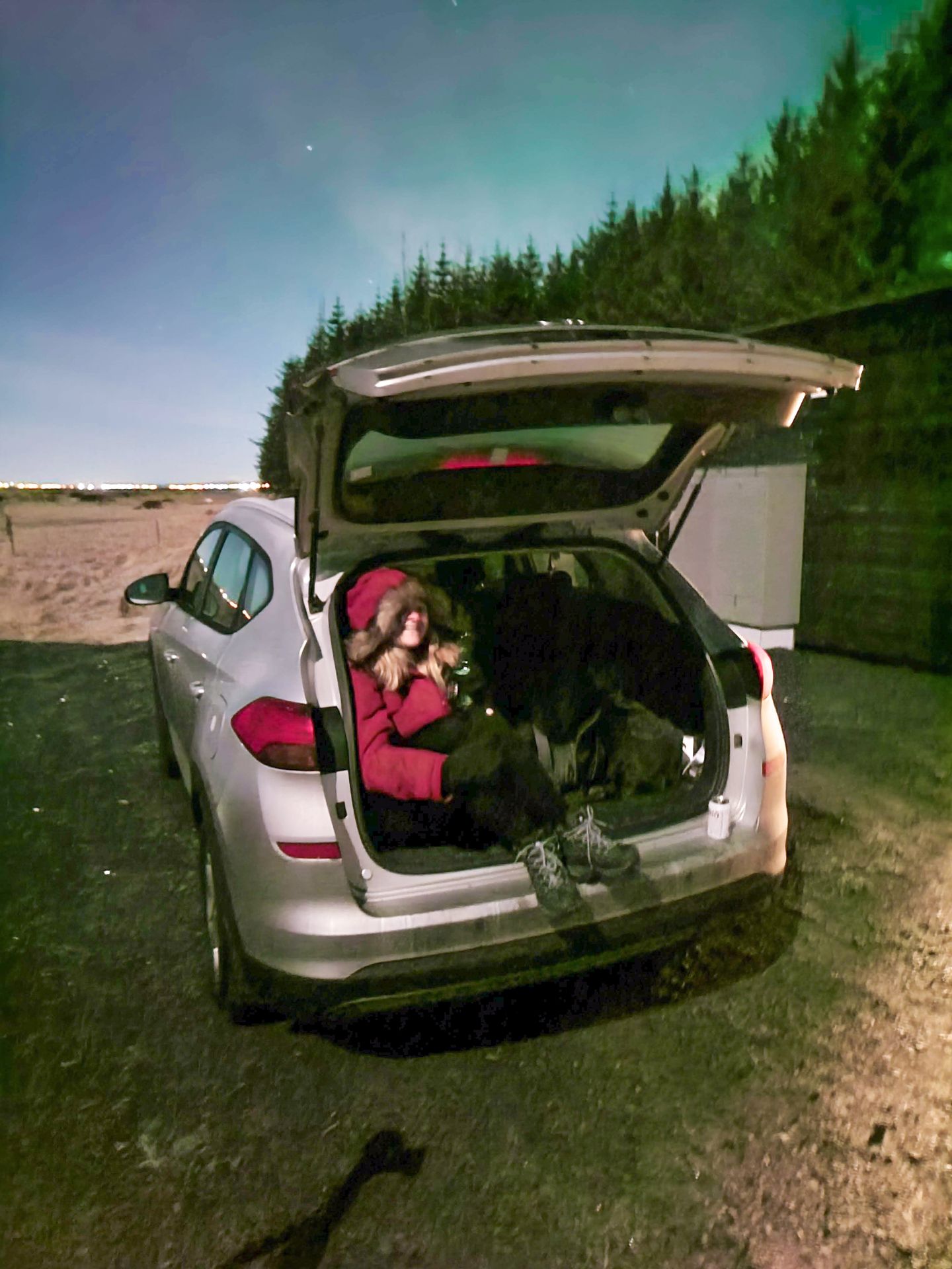 Lydia sitting in the truck of a small car while watching the Northern Lights in Iceland.