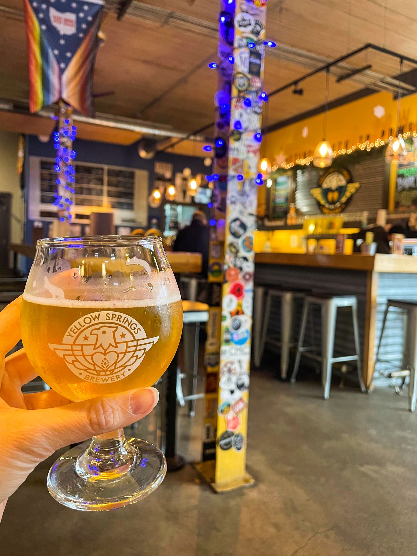 Holding up a beer inside of Yellow Springs Brewery. A column in the background is covered in stickers.