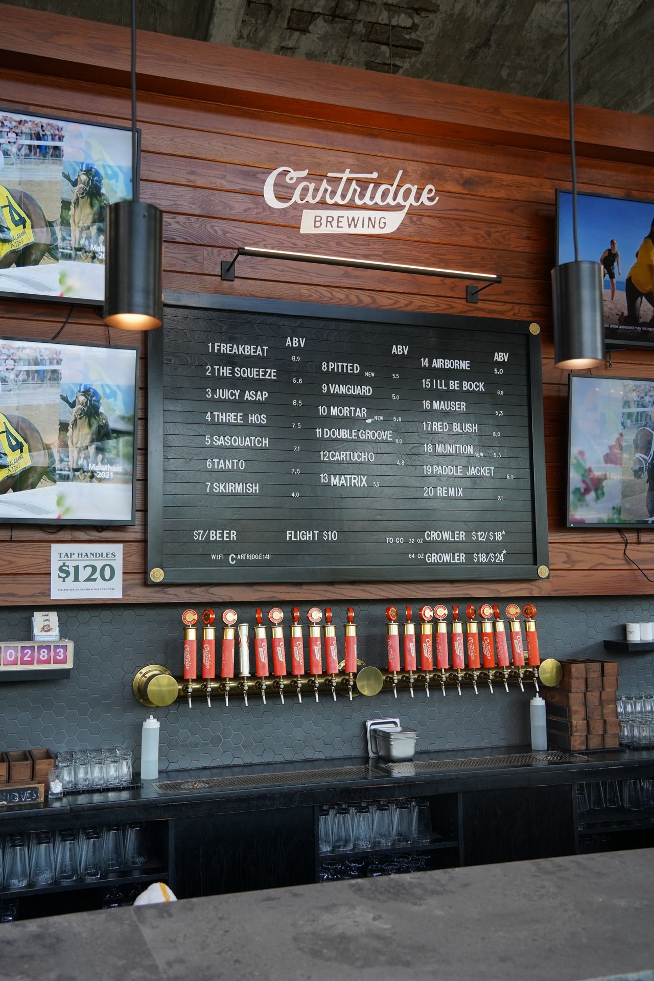 The taps at Cartridge Brewing. There is a wooden wall with a black message board lisiting the beers, and the taps are all orange.
