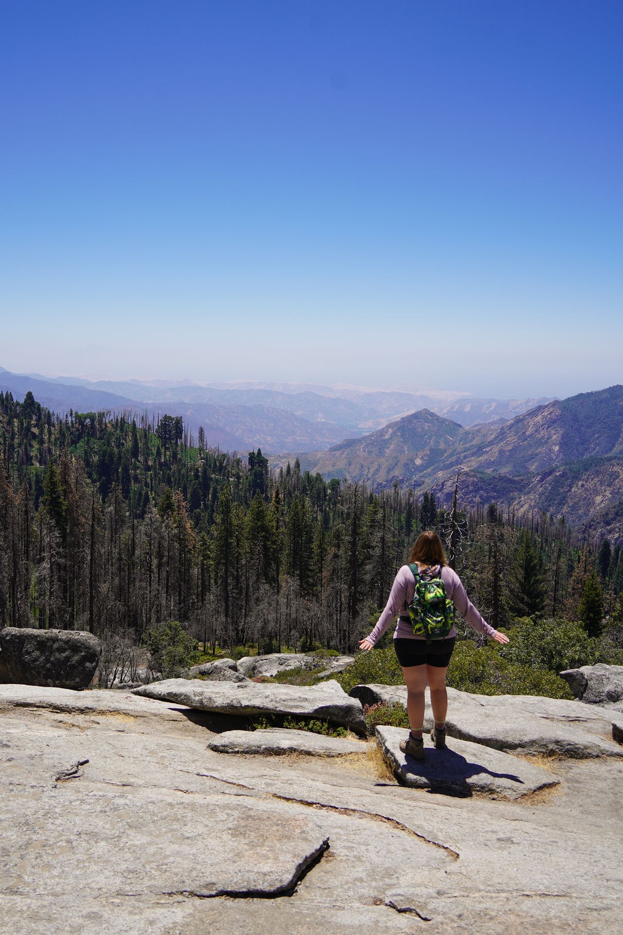 Lydia looking out at mountains and trees from a granite rock