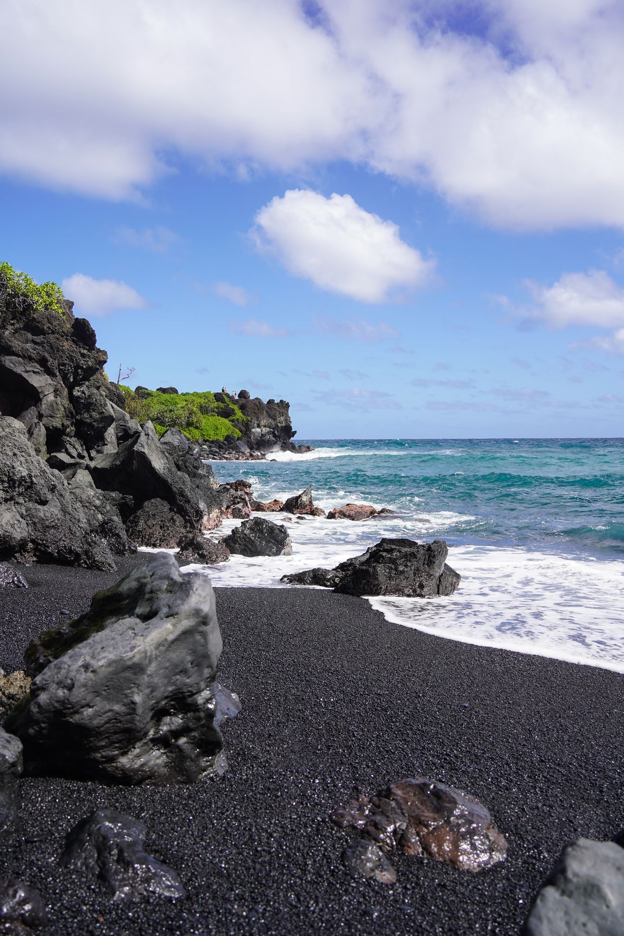 A black sand beach in front of a coast made up of black rocks