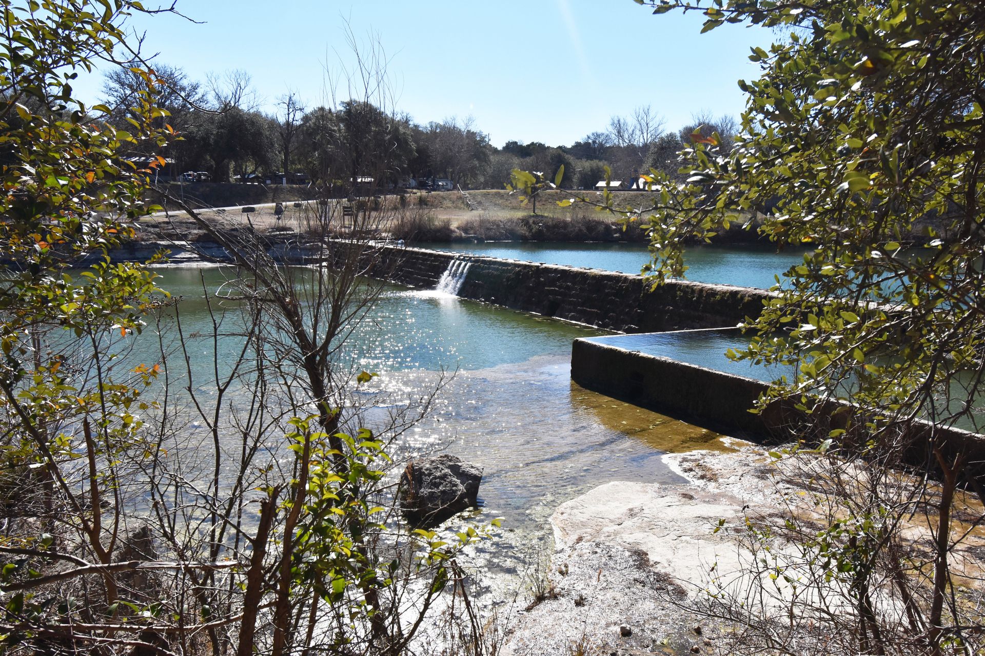 The swimming area of Blanco State Park, which has a dam with a small waterfall flowing over it.