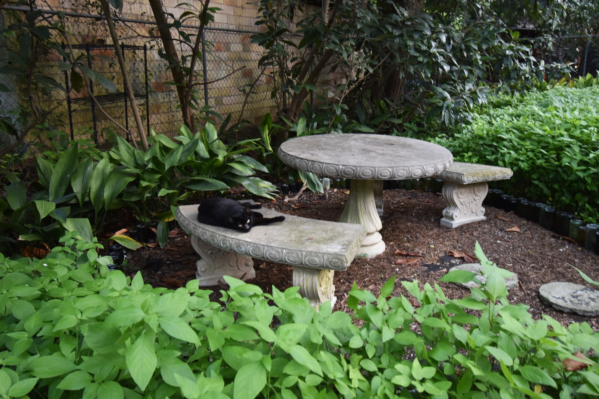 A stone picnic table with a black cat laying on the bench.