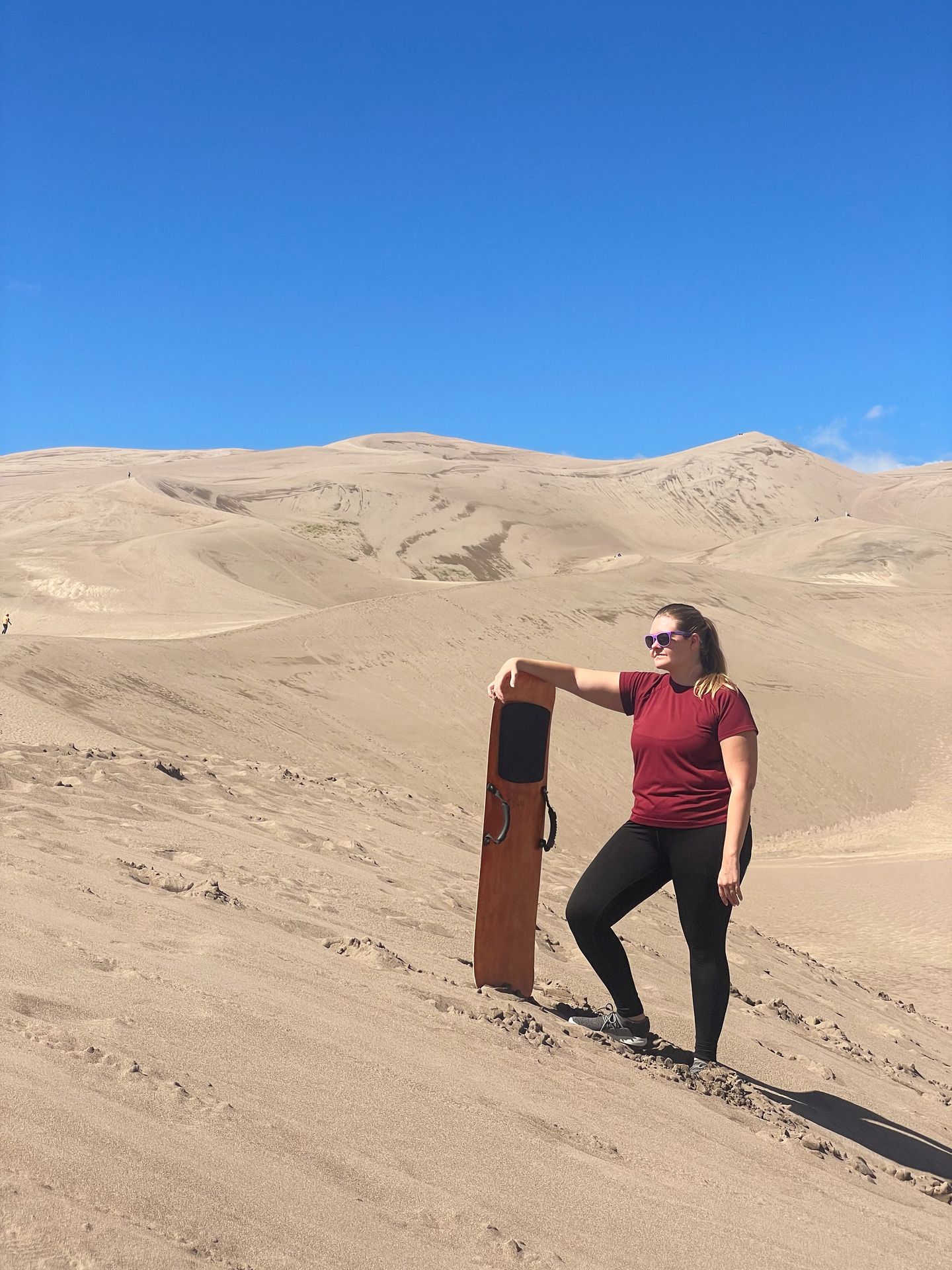 Lydia leaning on a sand board in Great Sand Dunes