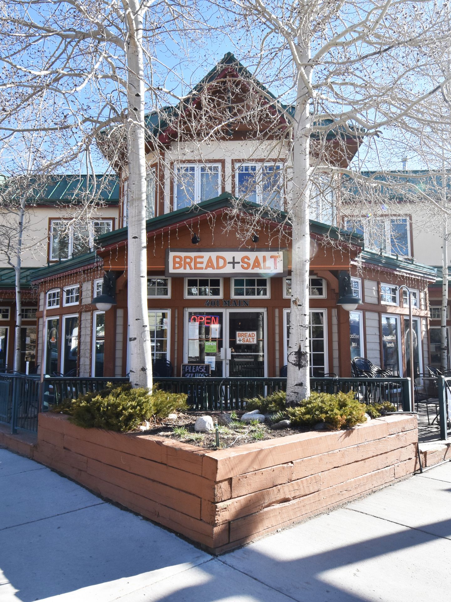 The outside of Bread and Salt. It sits on a corner and two white aspen trees frame the center of the building.