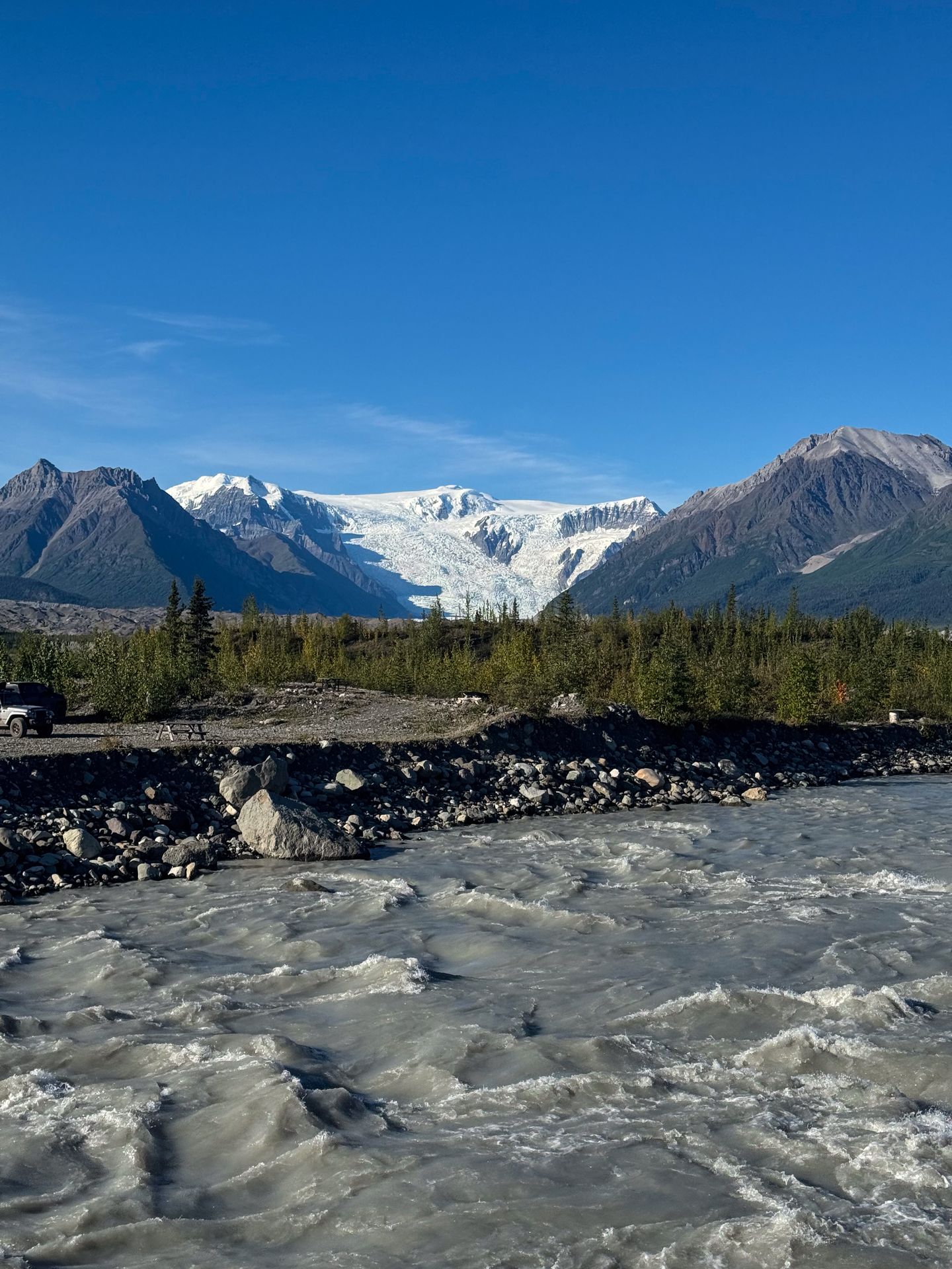 A view of a glacier and a flowing river seen from the footbridge to McCarthy