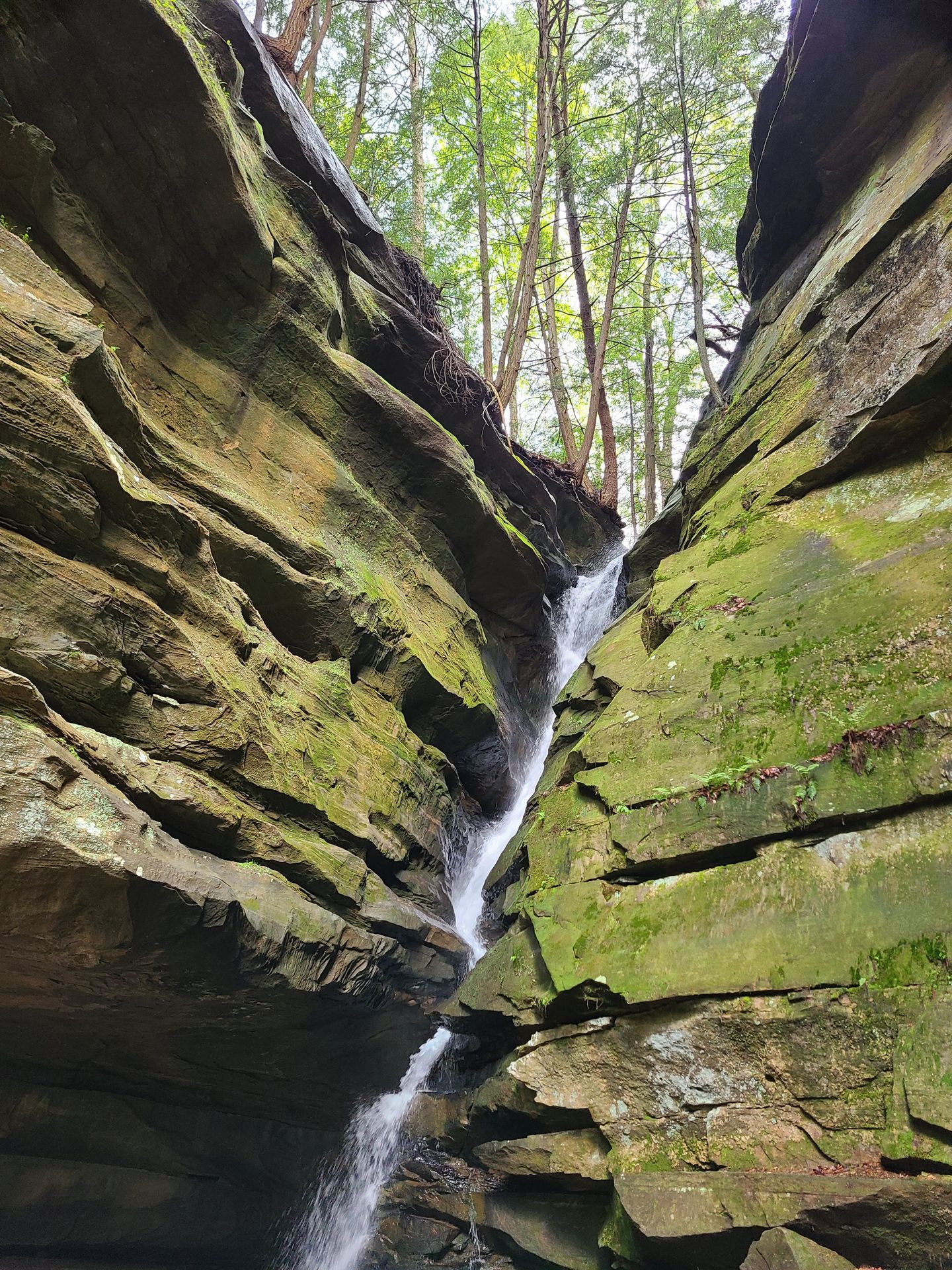 A thin waterfall between two large rocks covered in green moss.