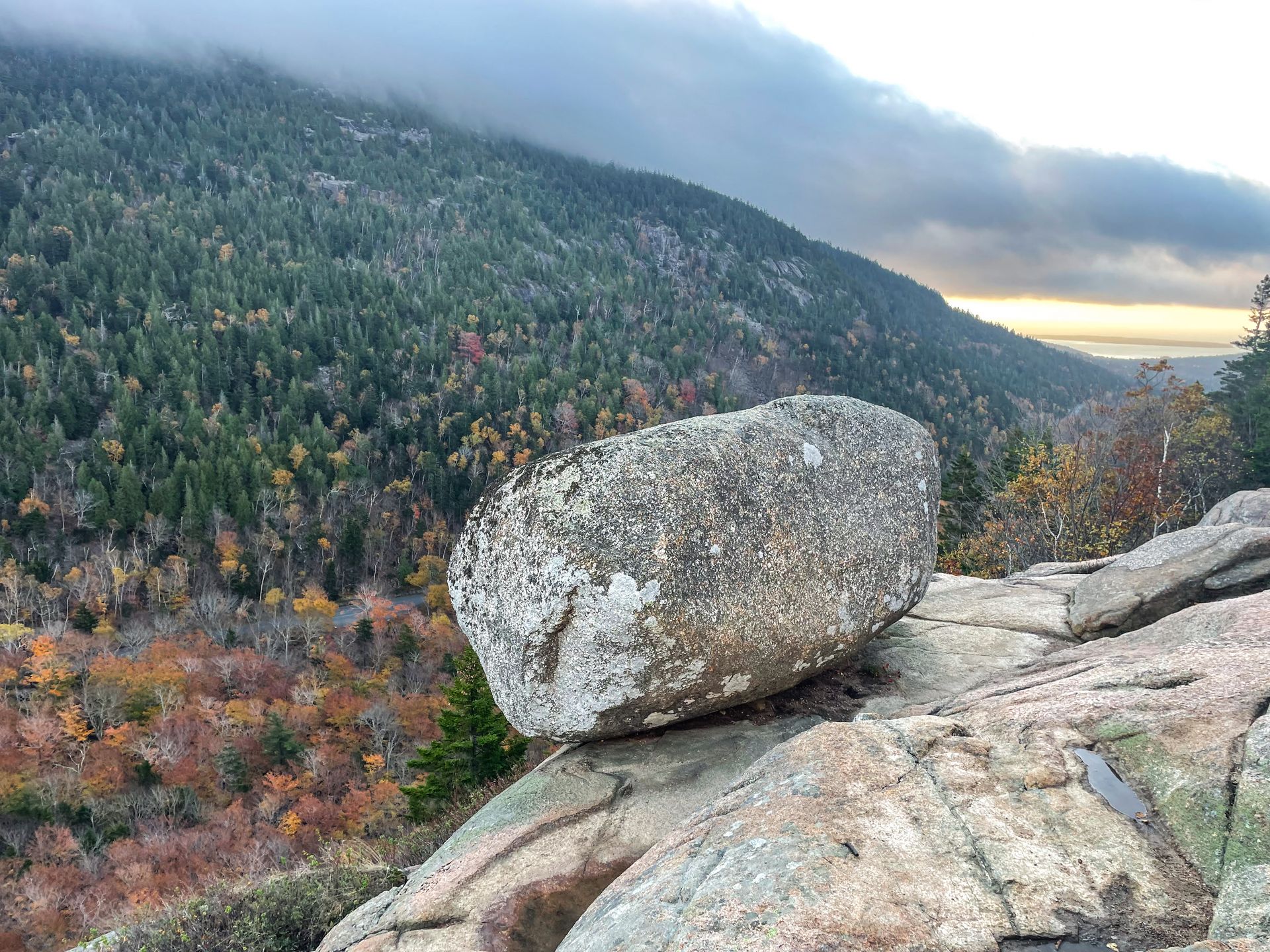 A huge boulder sitting on the edge of a cliff.