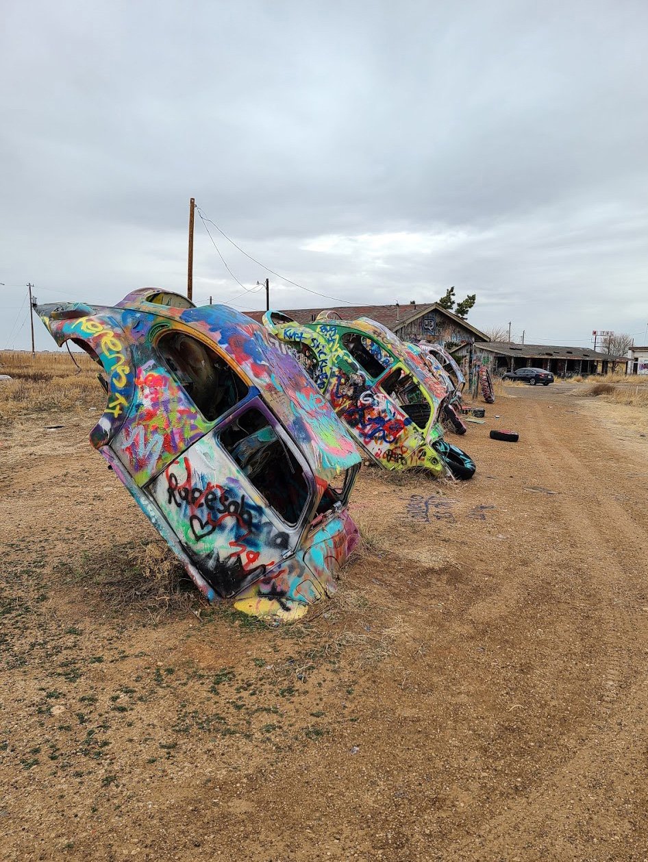 An angled view of a few painted volkswagen beetles in a row.