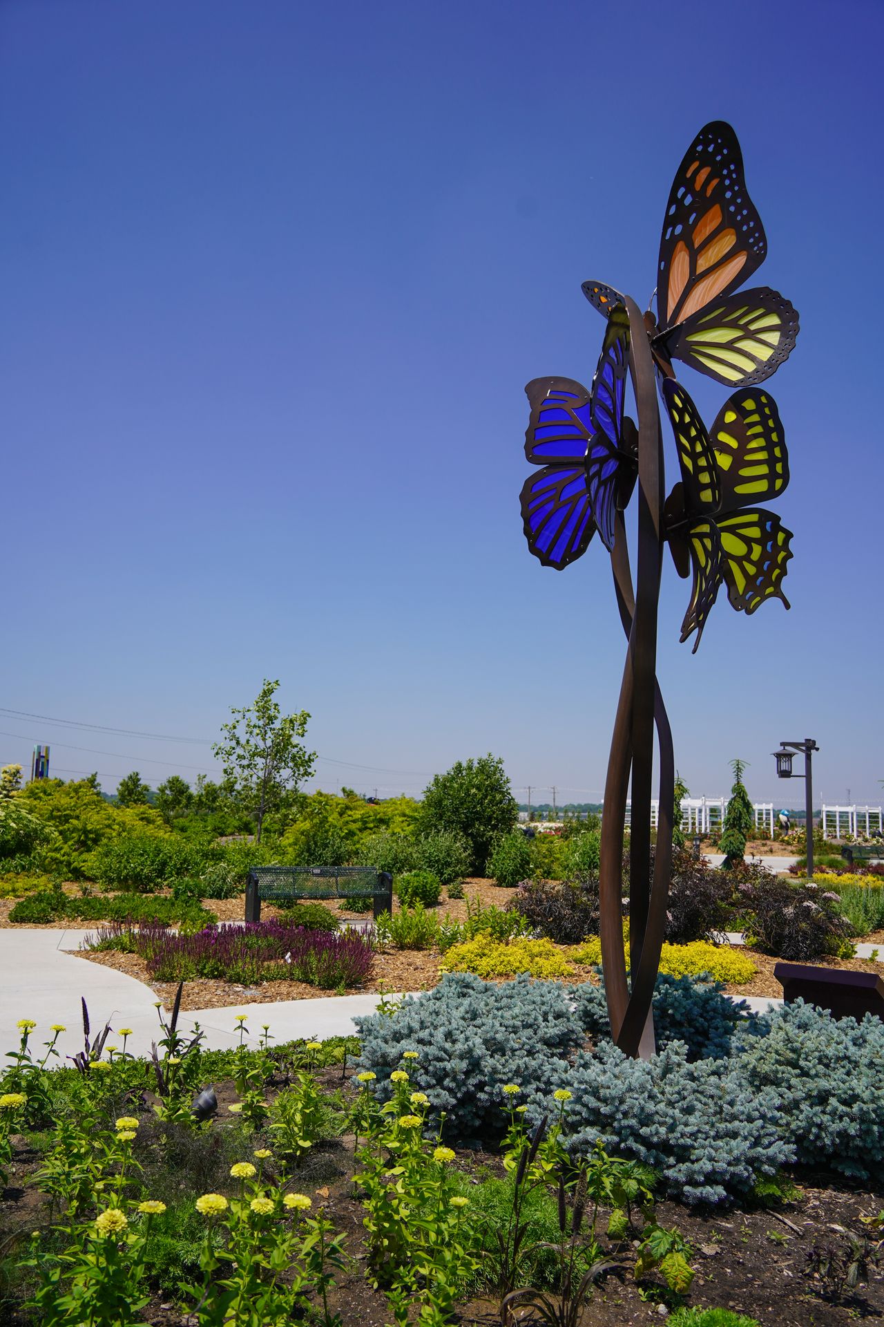 A tall butterfly sculpture among flowers and sidewalks at Yanney Heritage Park