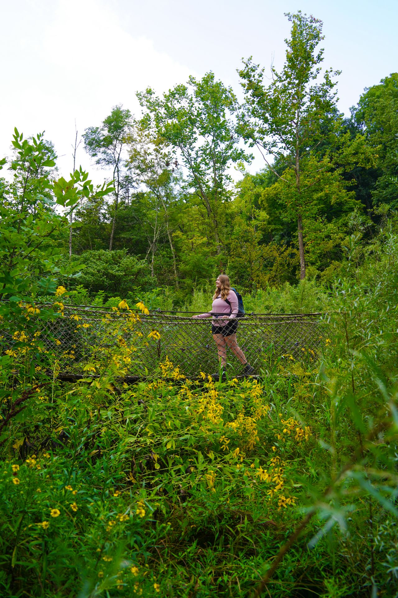 Lydia on a swinging bridge that is surrounded by greenery and yellow flowers