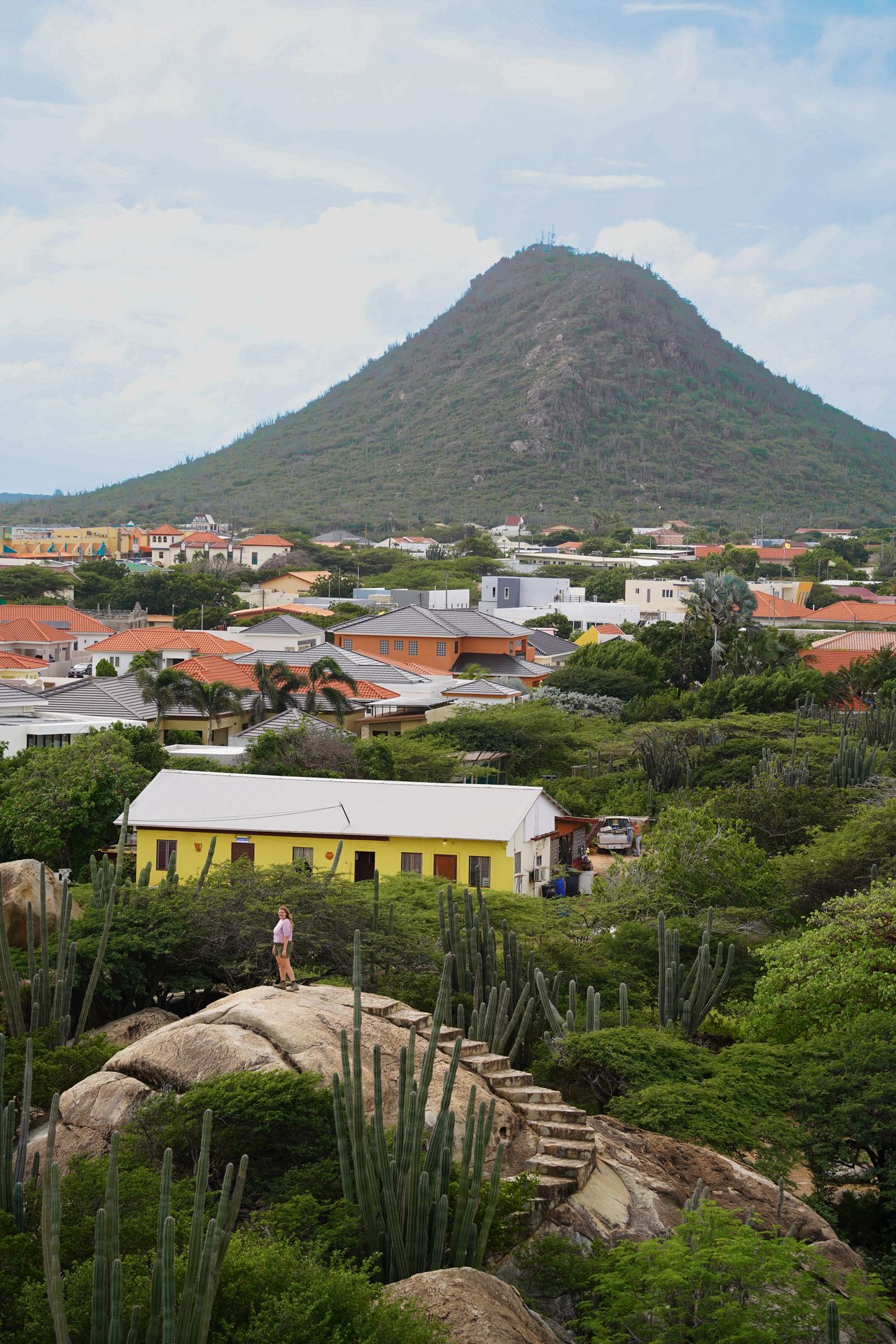 Lydia on top of a rock with steps built into it. A large, cone-shaped hill is in the background.