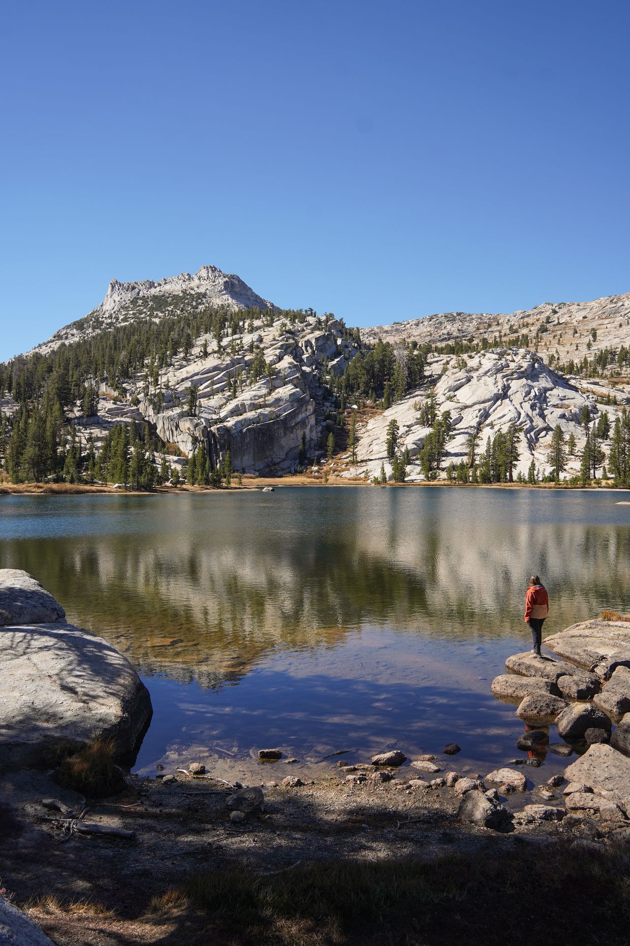 Lydia standing on the shore of Upper Cathedral Lake, where a peak is reflecting in the water