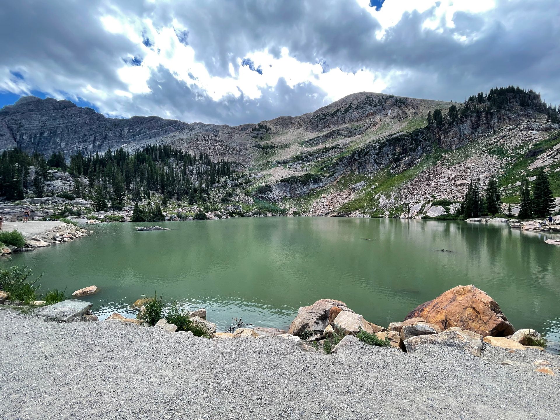 A green colored lake with a rolling mountain top behind it.