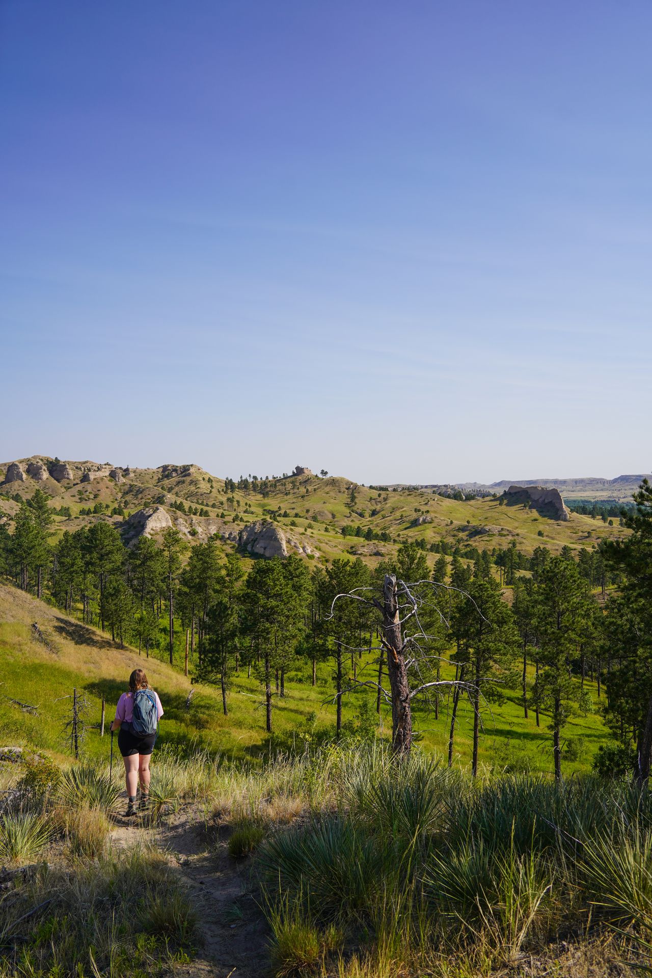 Lydia on a hiking trail in Chadron State Park, with views of rocks and green hills in the distance