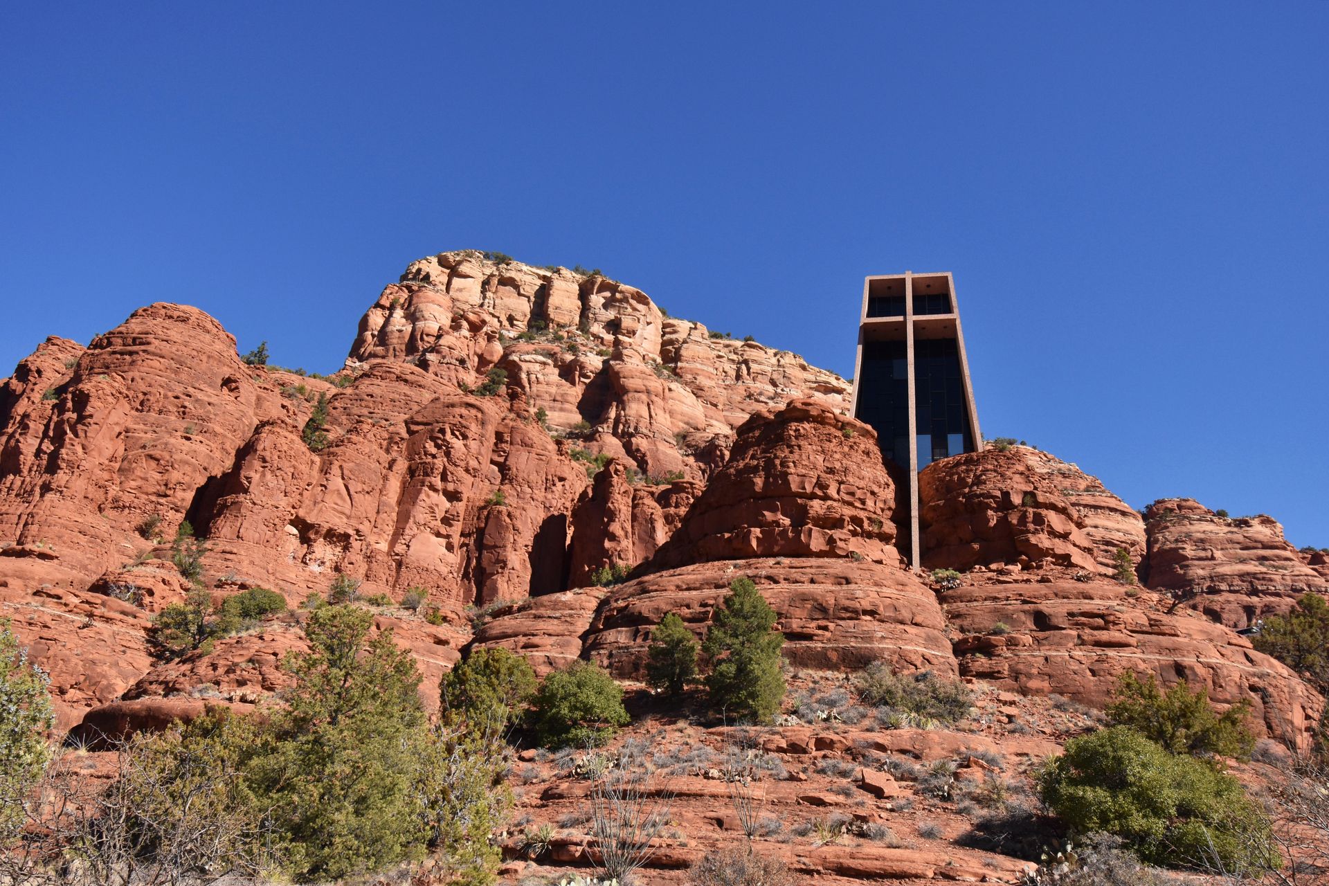 Looking up a glass chapel that rises up from orange rock faces. There are other orange rock faces in the background.