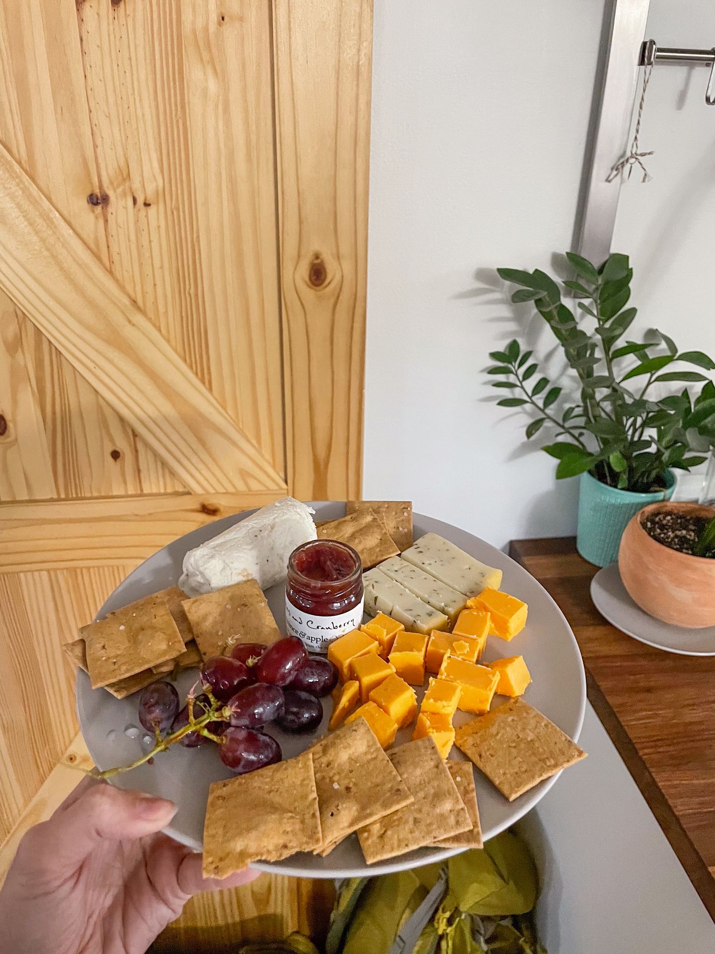 A homemade cheese plate with 3 cheeses, grapes, crackers and a jam bought from Fromagination